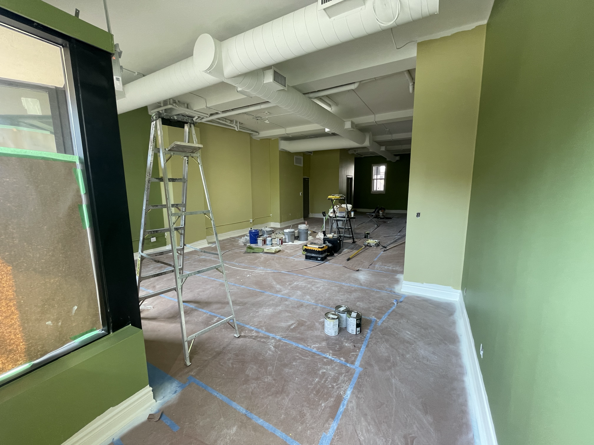 Interior room under renovation with green walls, a ladder, paint cans, and tools. Commercial Painting. Heather Feather Painting and Design. Toronto. 