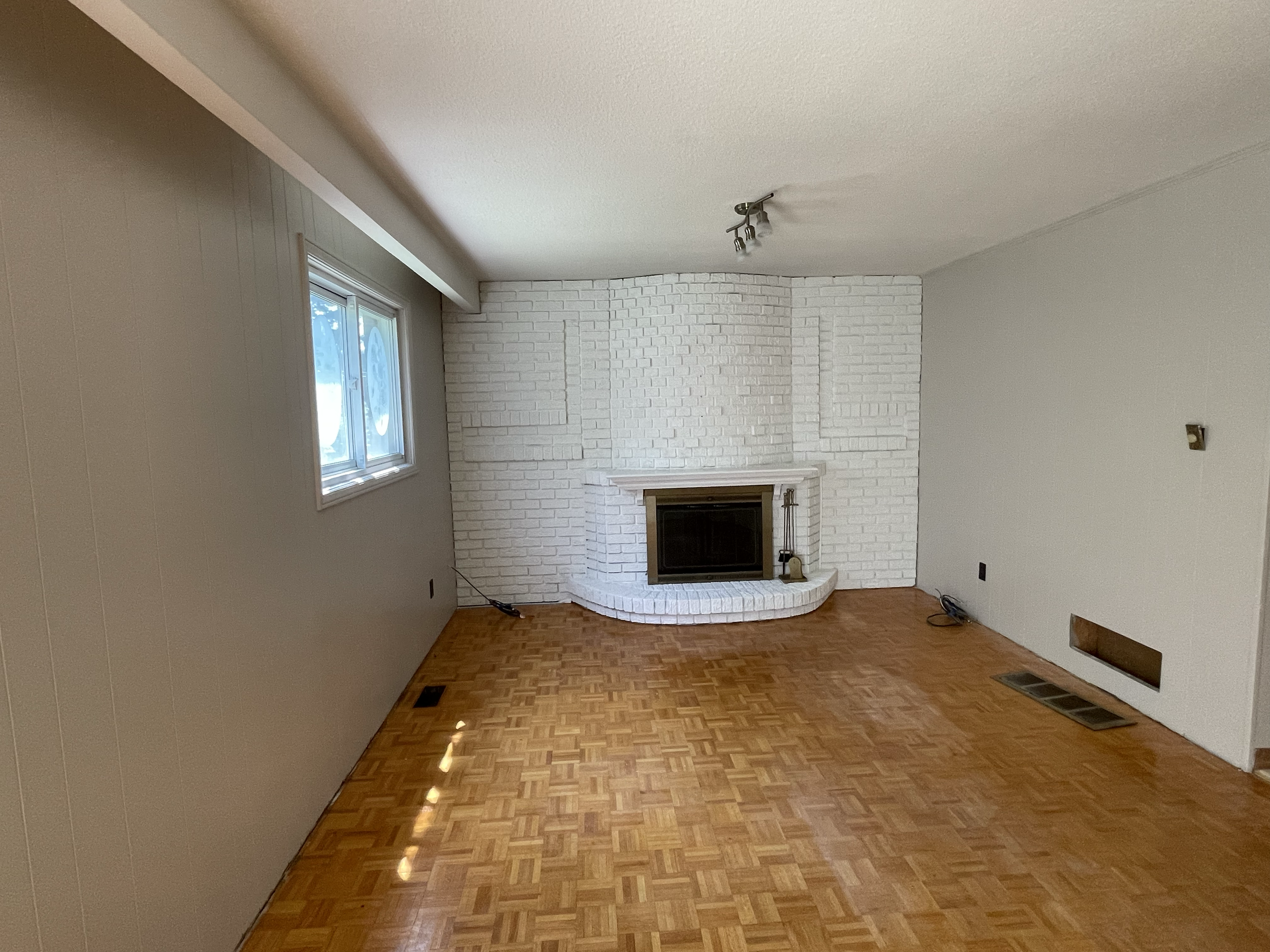 Living room with white brick fireplace, large window, hardwood floor, and neutral-colored walls.Interior House Painting. Heather Feather Painting and Design. Toronto. Spraying. Fireplace. Paneling 