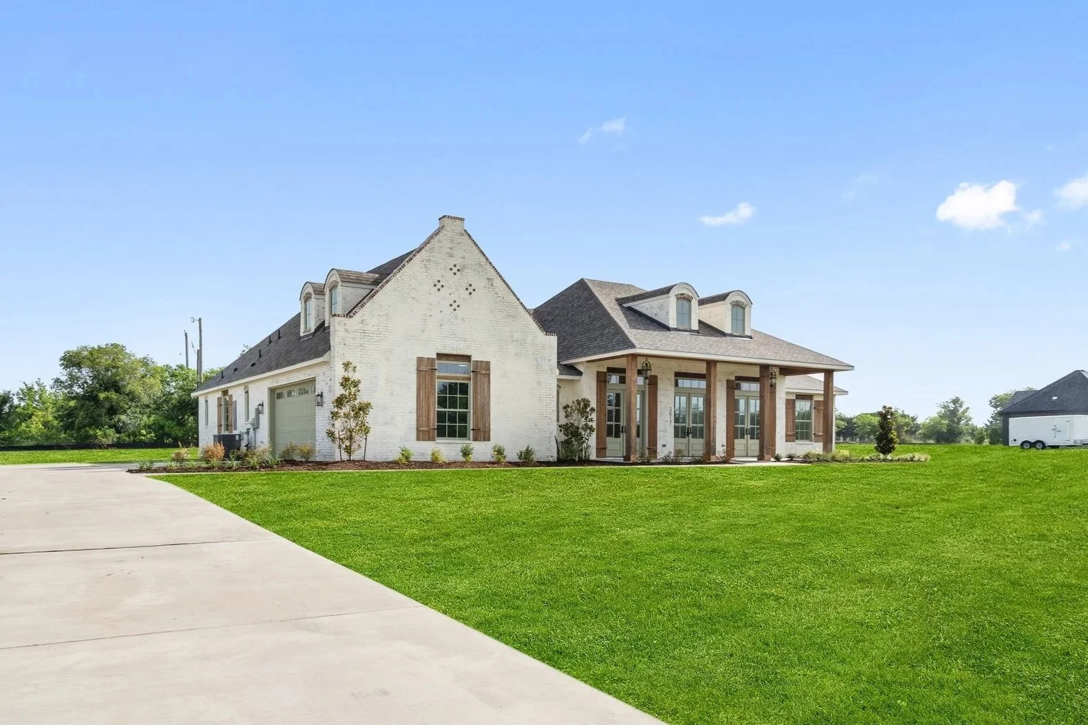 A modern suburban house with a large lawn, driveway, and a porch with columns, under a clear blue sky.