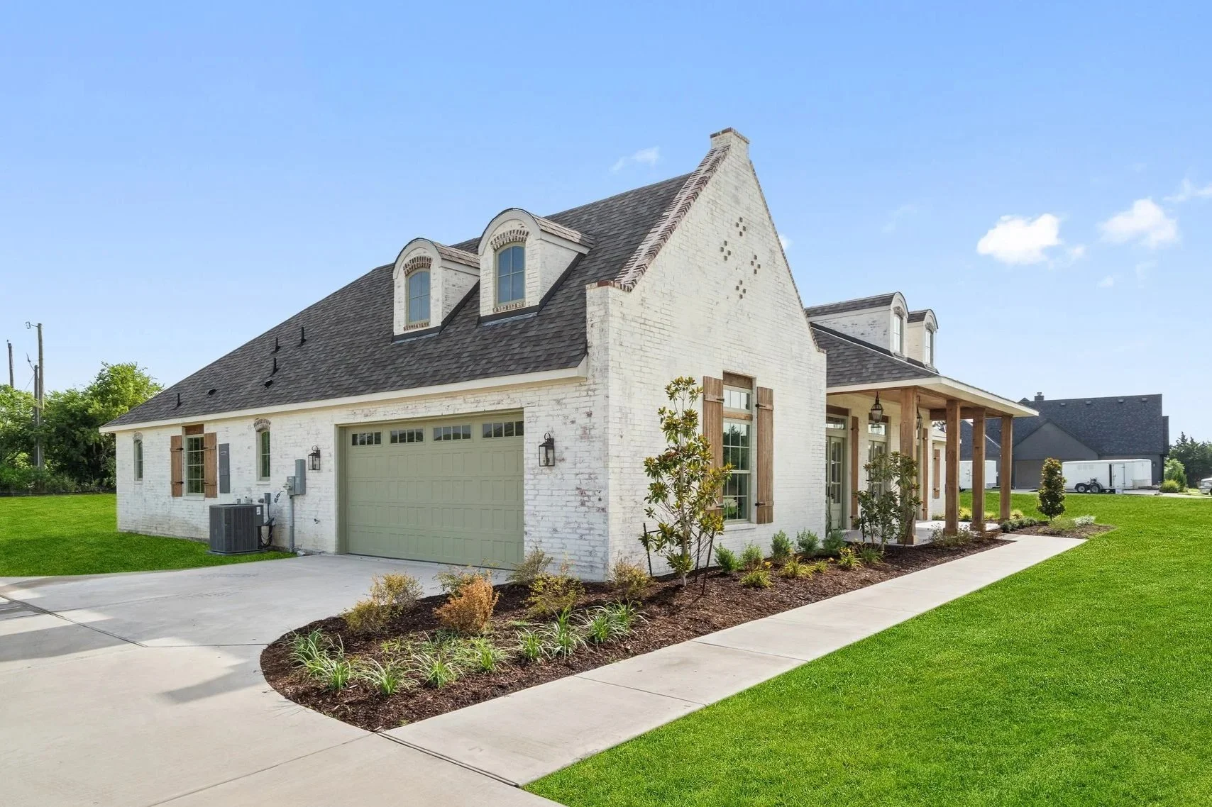 A modern white brick house with a two-car garage, small front porch, and landscaped yard on a sunny day.