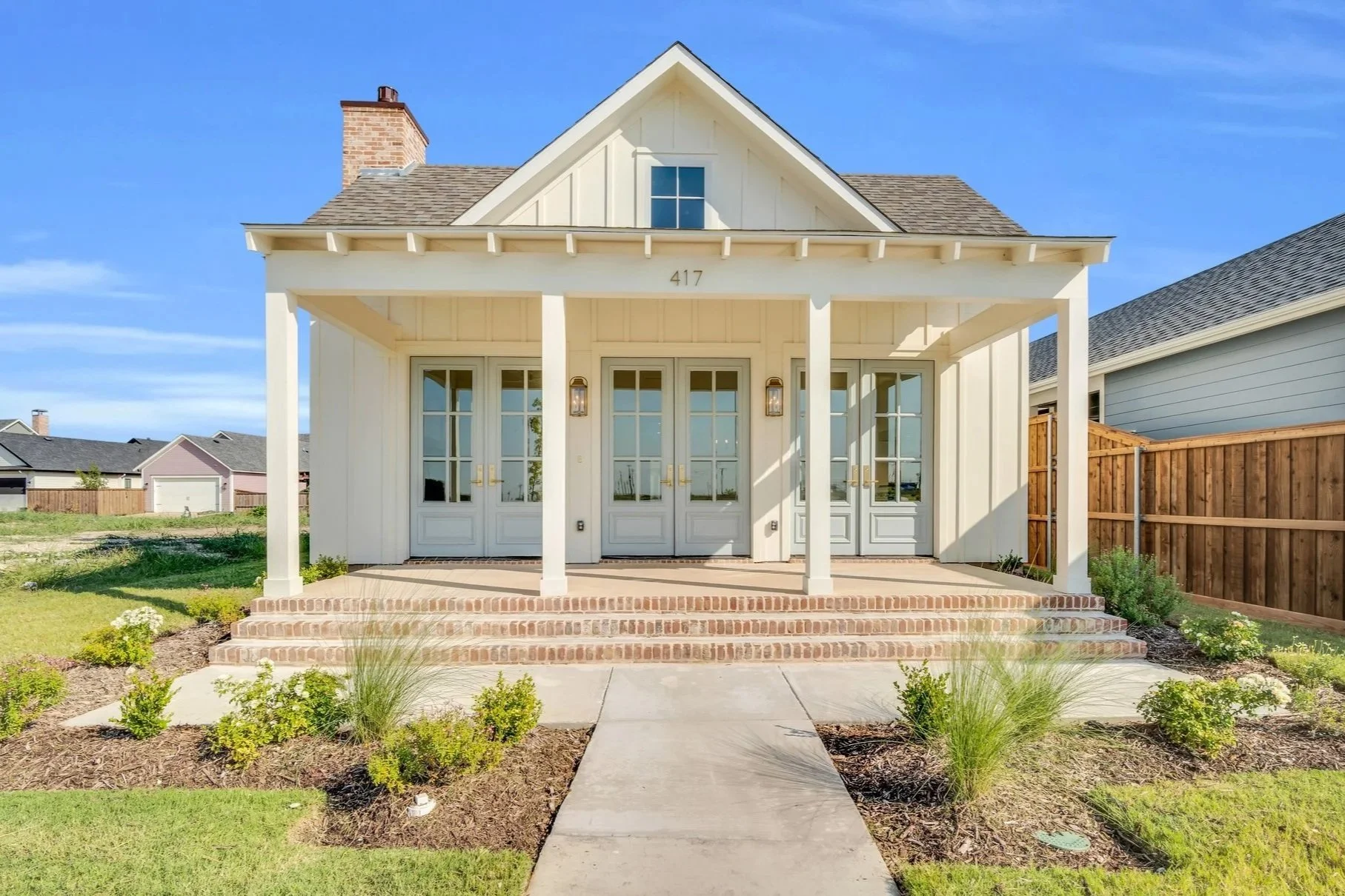 A white house with a covered porch, brick steps, front door with glass panels, and a gable roof under a blue sky.