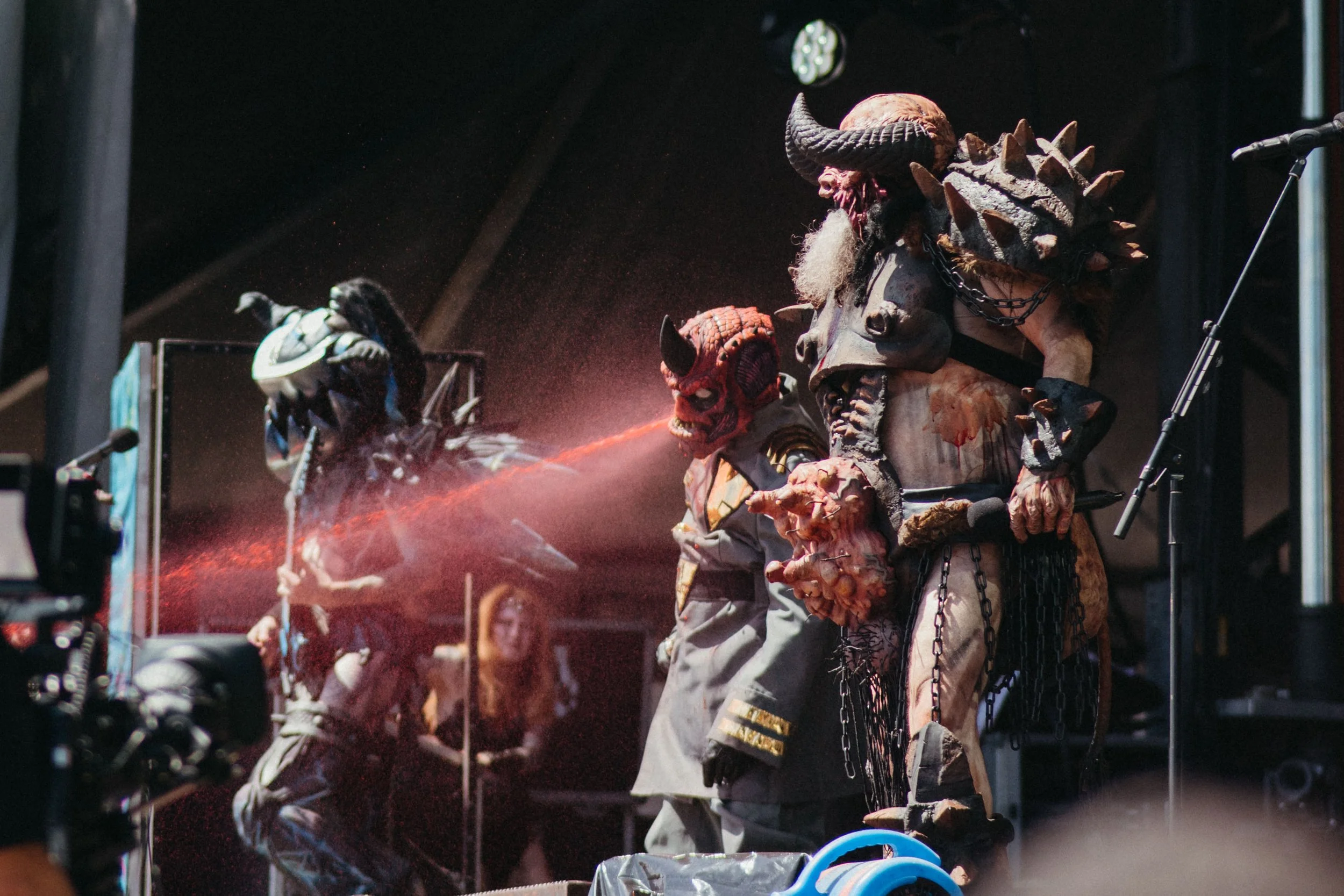 Costumed performer dressed as a creature with horns, spikes, and chains on stage, with bright red lighting effects.
