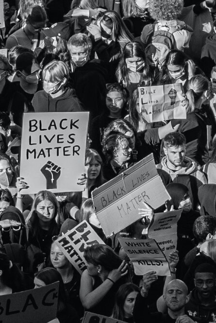Black and white image of a large, diverse group, many of which are holding Black Lives Matter signs and wearing COVID masks.