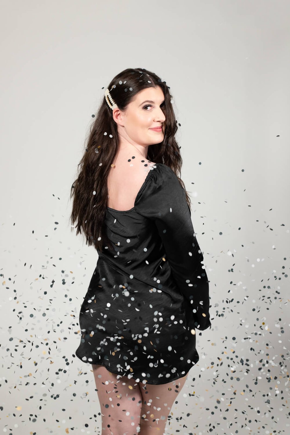 young woman in black dress with confetti falling on New Years eve