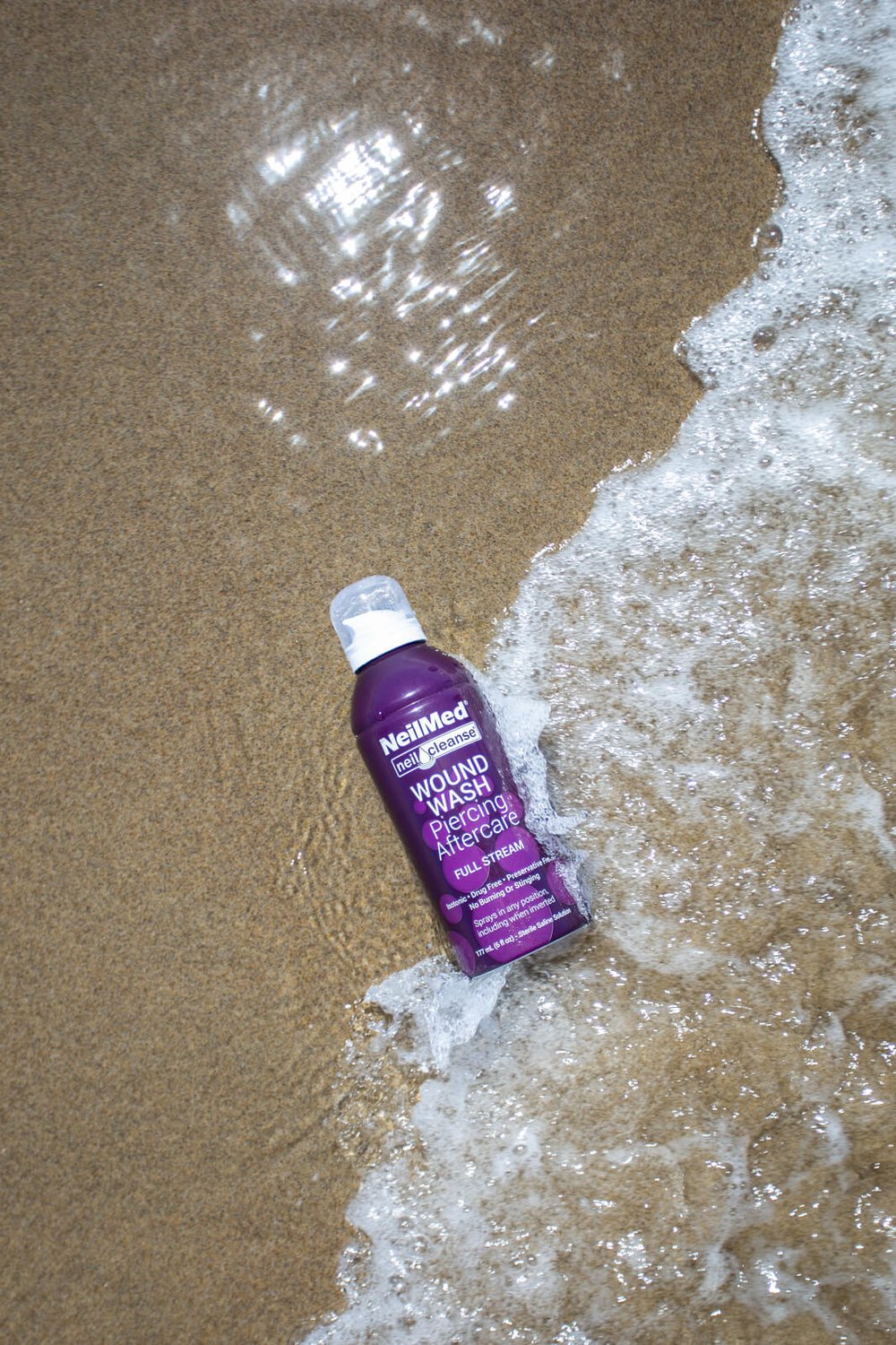 piercing aftercare bottle being splashed by ocean waves on beach