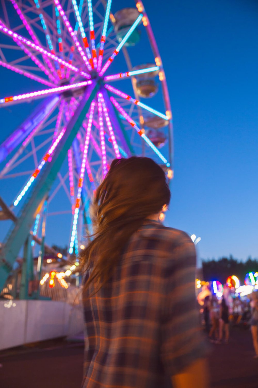 long exposure of brunette woman in front of ferris wheel at fair