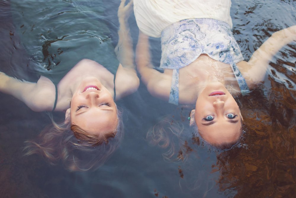 two women float in river with dresses on