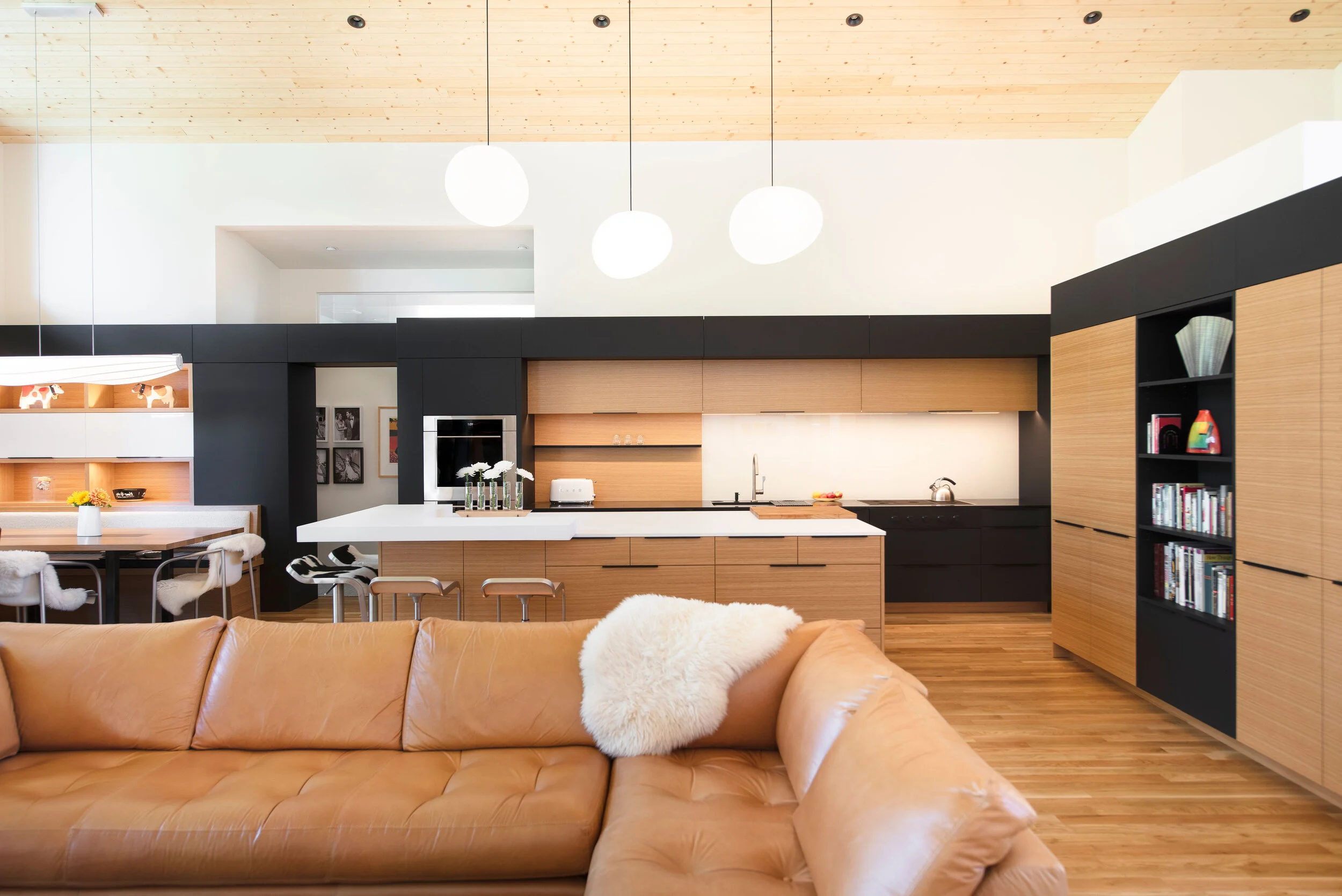 Modern open-concept kitchen and living space with custom wood cabinetry, minimalist black accents, pendant lighting, and hardwood floors, renovated by Copperline Homes in Central Oregon.
