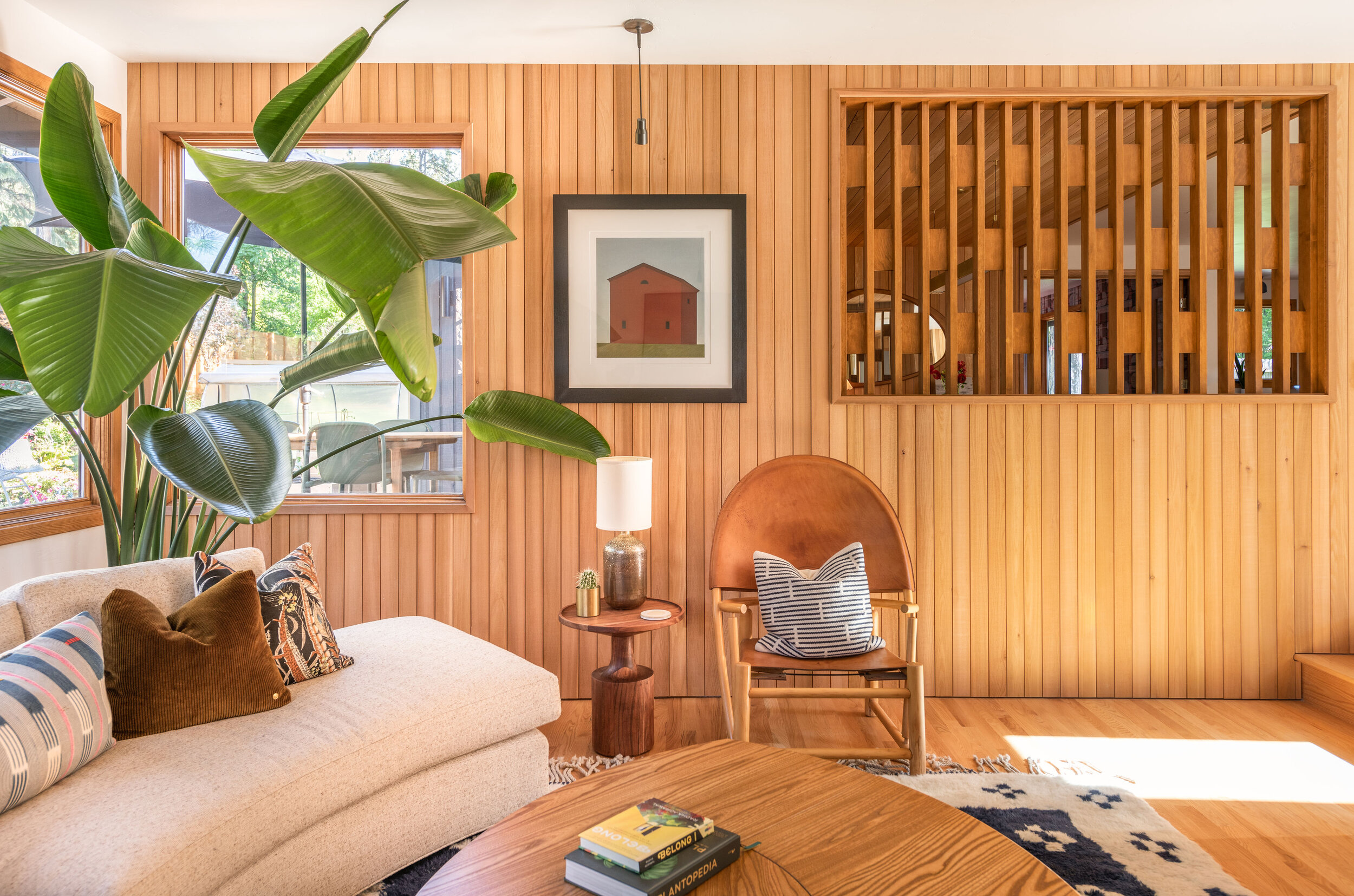 Midcentury-inspired living room with vertical wood paneling, modern furniture, large indoor plant, and natural light, part of a custom interior renovation by Copperline Homes in Central Oregon.
