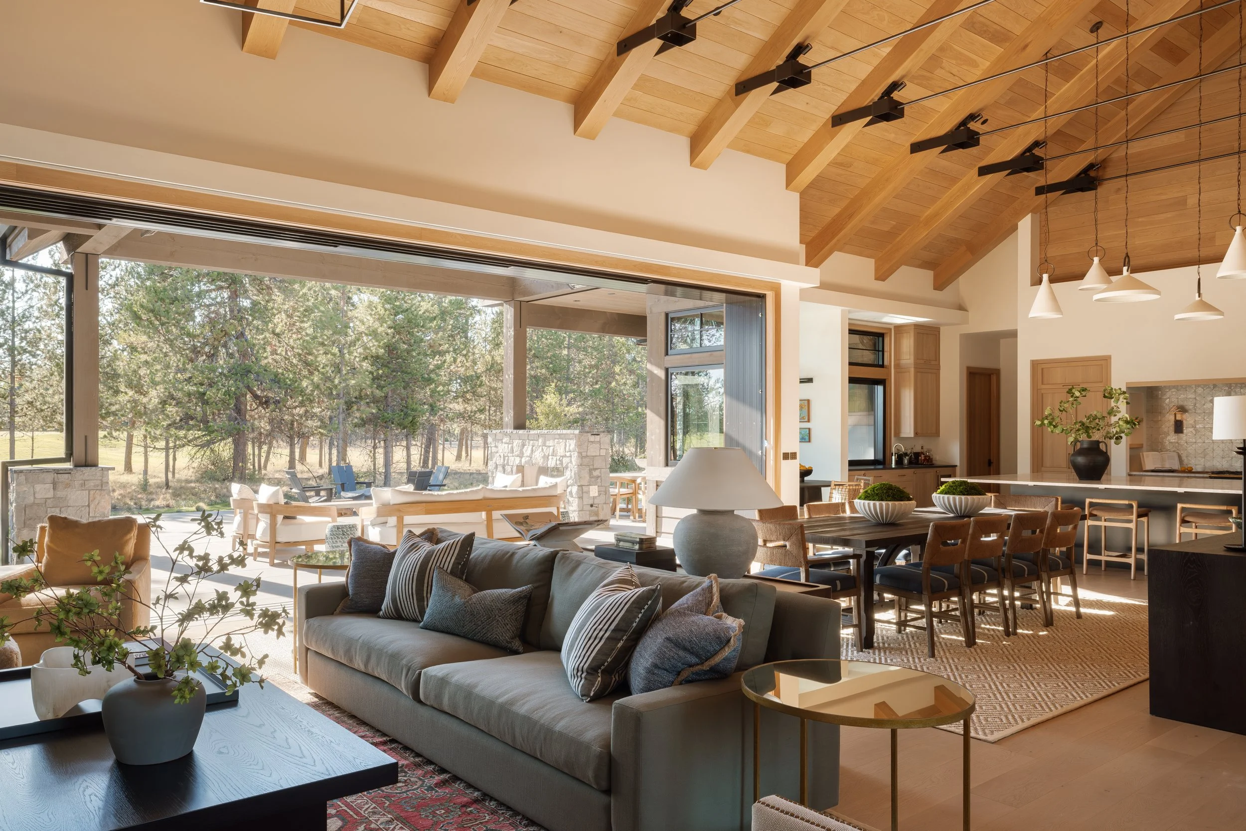 Living room with a wall of sliding glass doors opened up to the patio and pines.