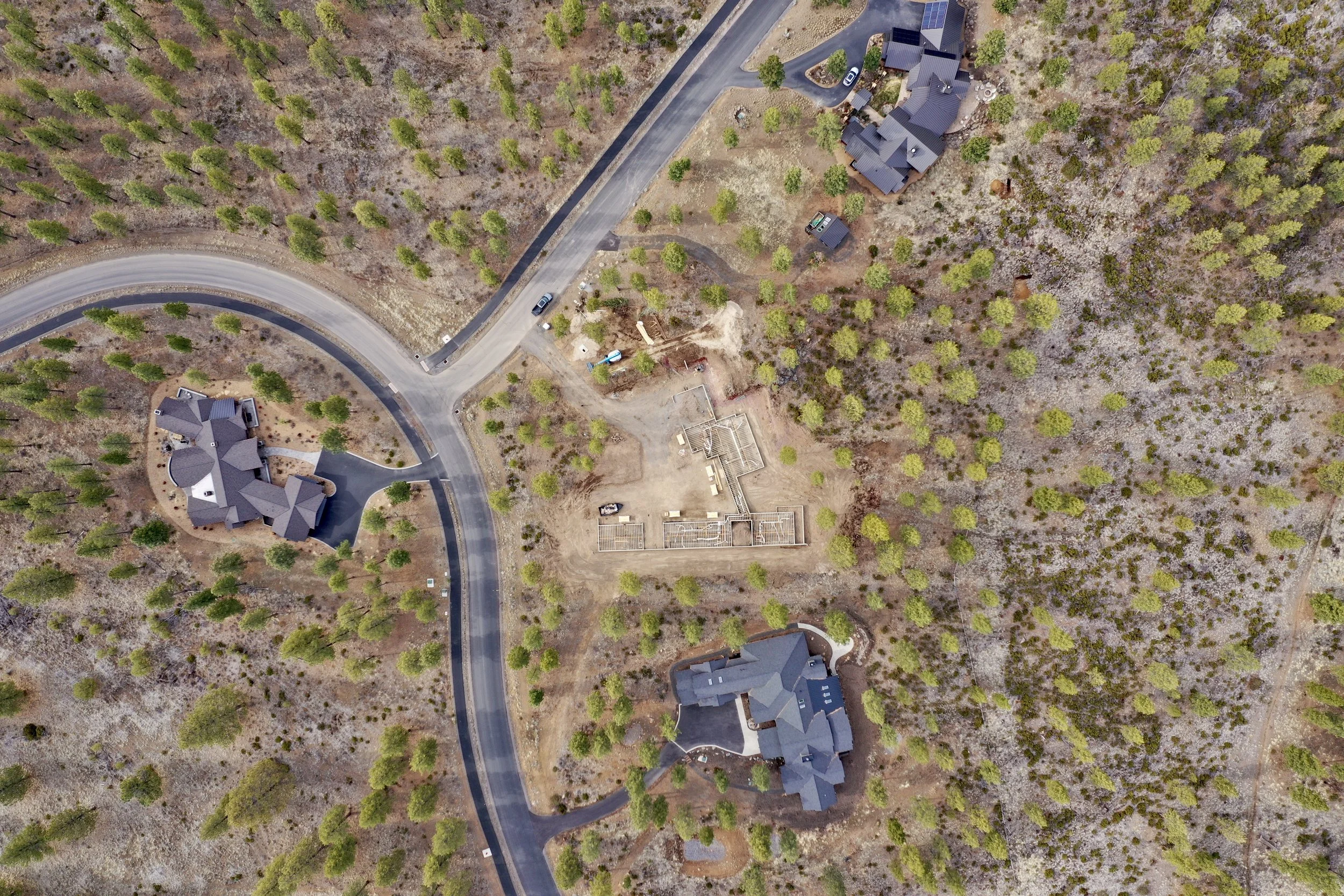 Aerial view of custom home construction site at foundation stage surrounded by completed homes and high desert landscape in Central Oregon