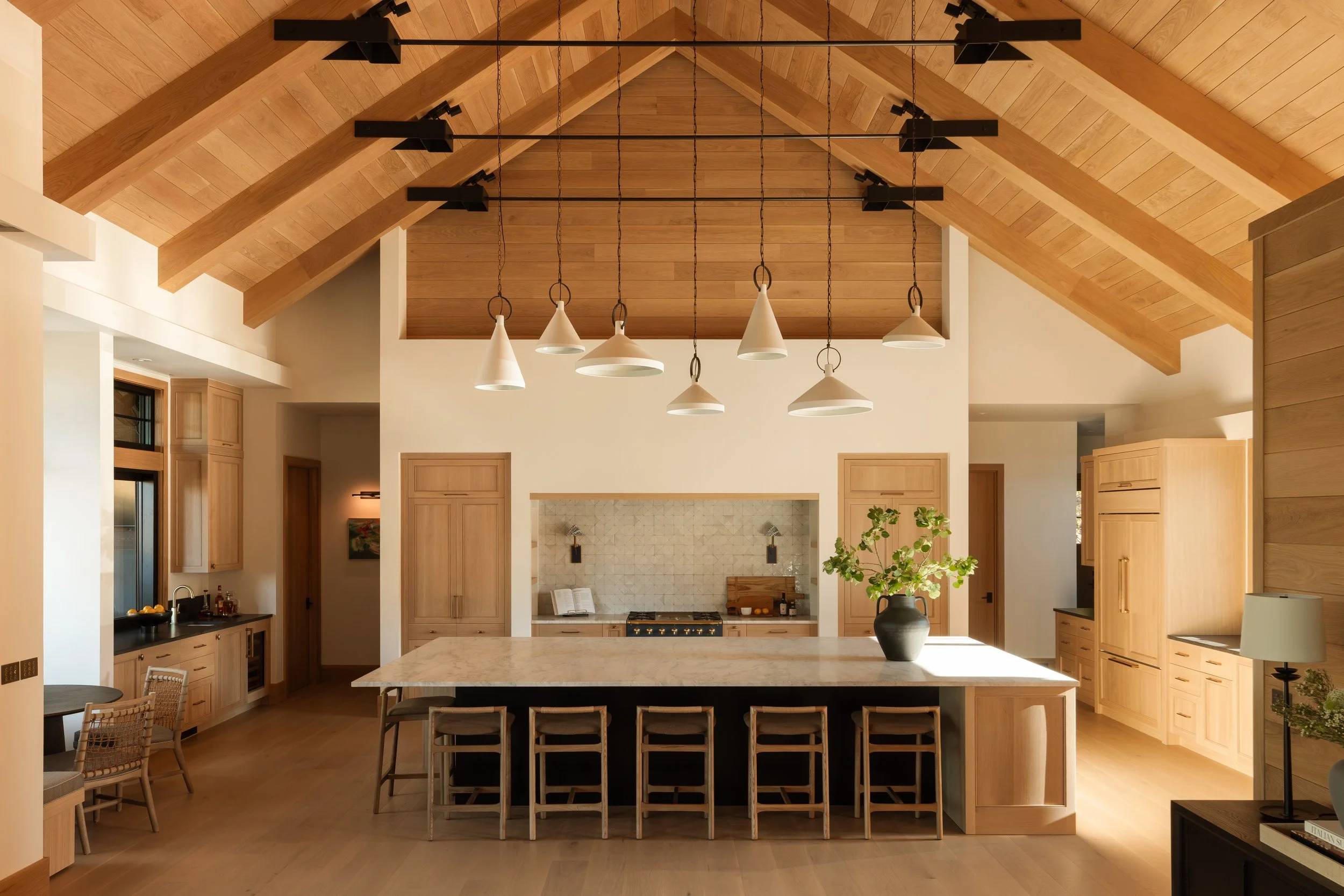 Kitchen under vaulted timber trusses with a long stone-topped island, in a Copperline custom home in Crosswater, Sunriver, Oregon.