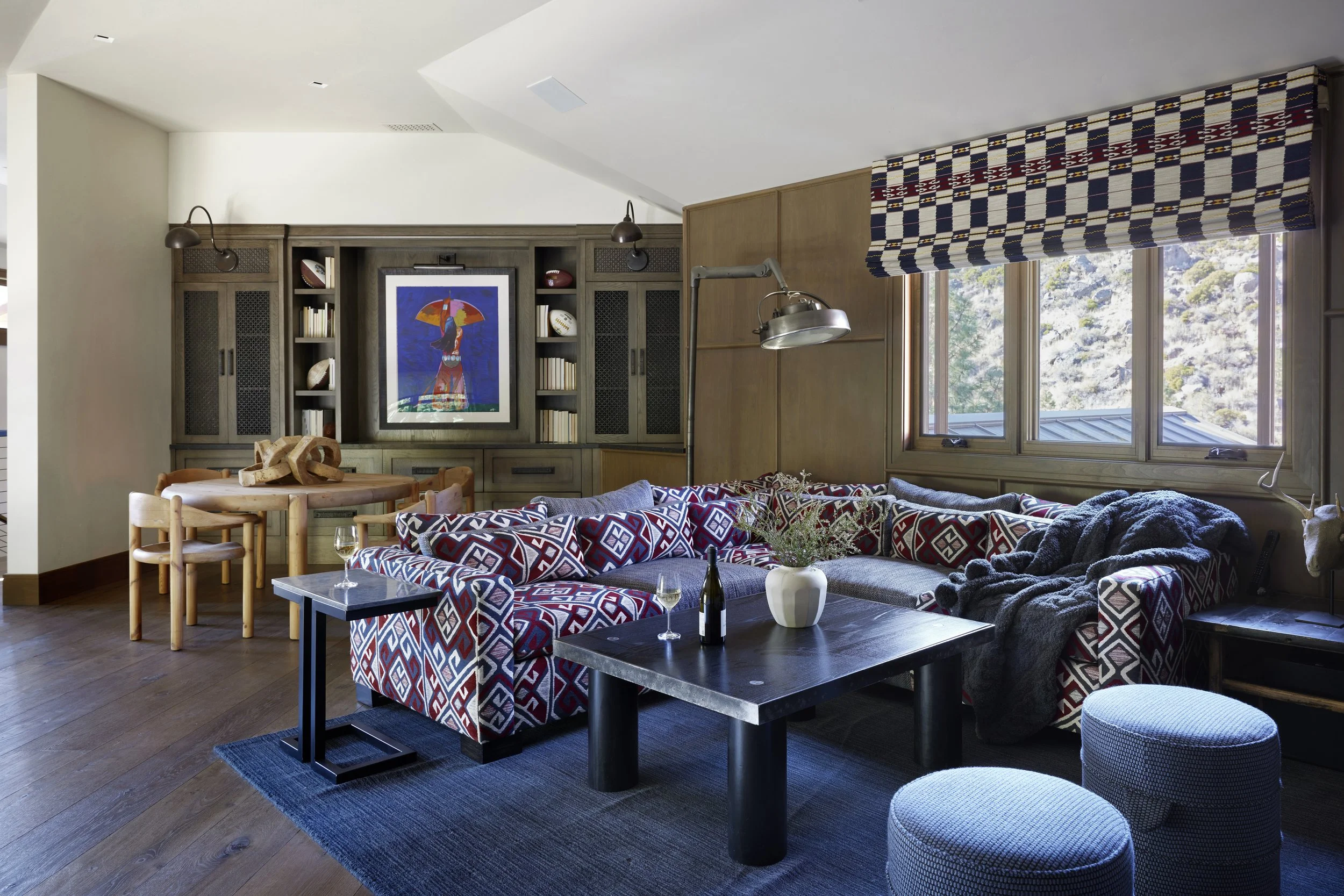 Living room with a sectional sofa, coffee tables, patterned cushions, and large window with a valance, overlooking trees.