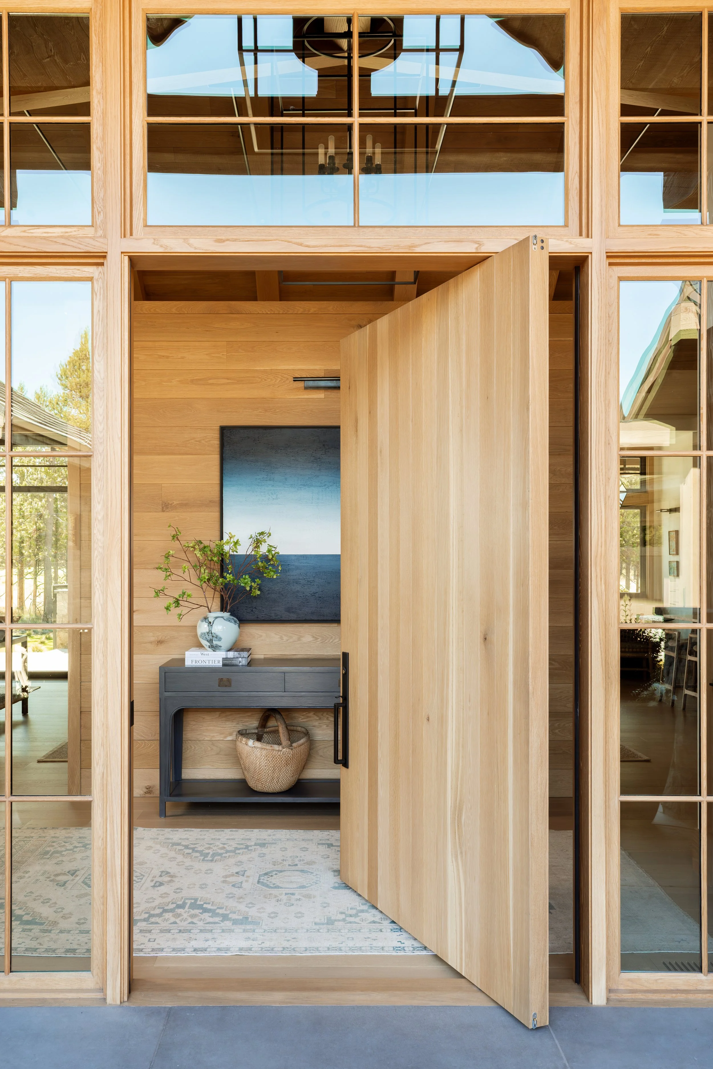 Tall wood pivot front door with glass sidelights and transoms.