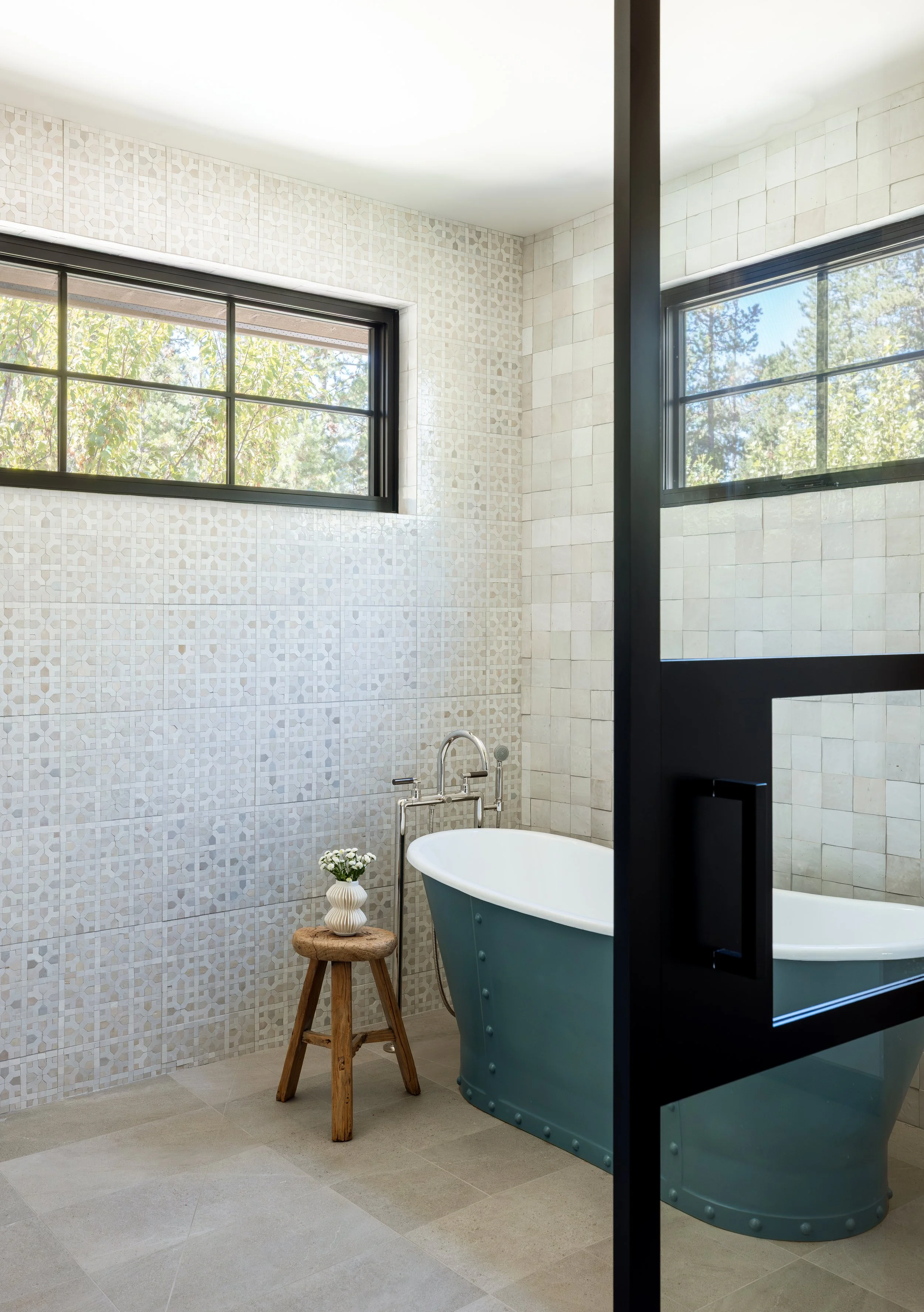 Master bathroom with a freestanding soaking tub behind steel-framed glass.