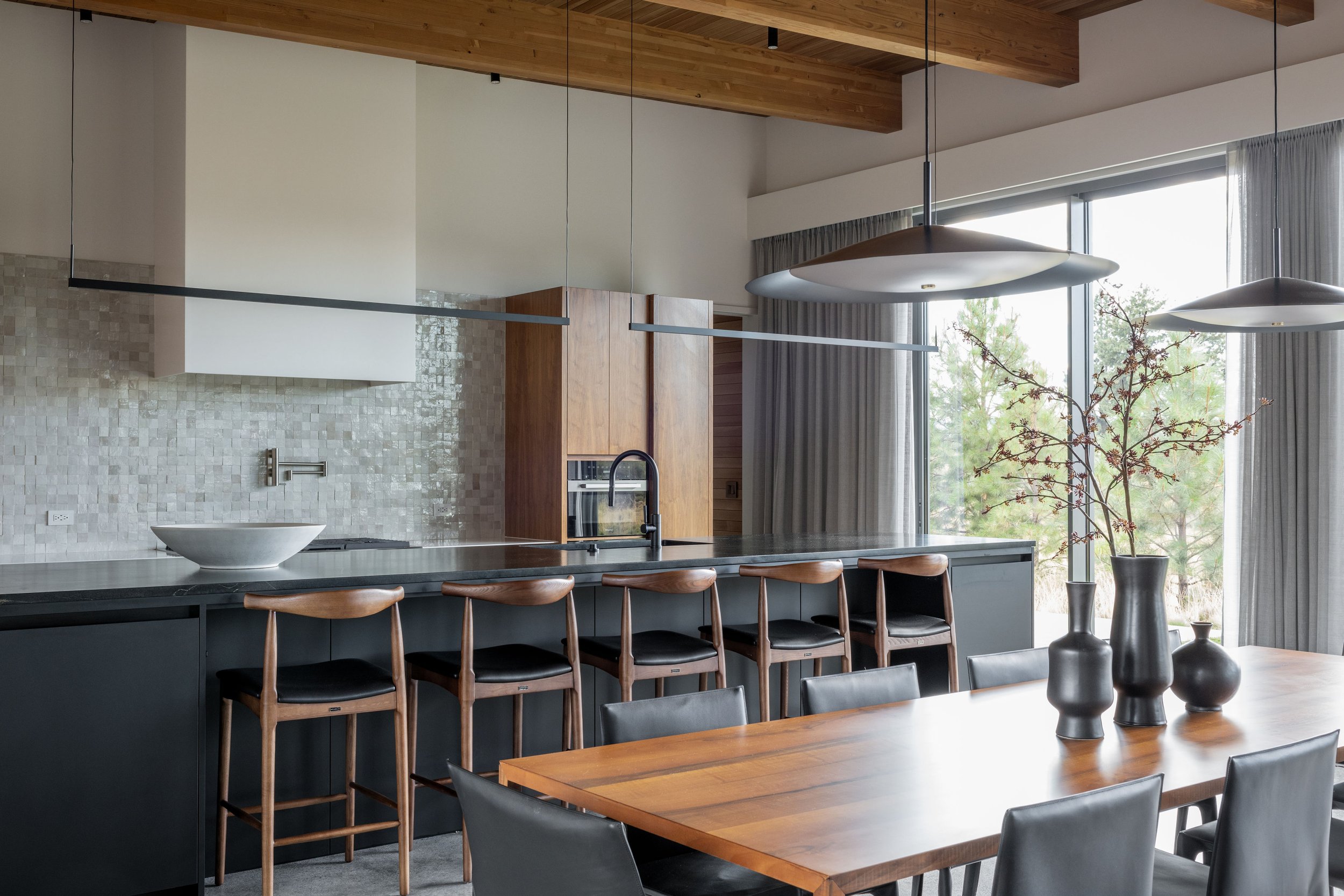 Modern kitchen with dark casework, soapstone countertops, zellige tile backsplash, walnut accents, mid-century bar stools, and exposed wood beam ceiling in a Bend Oregon custom home