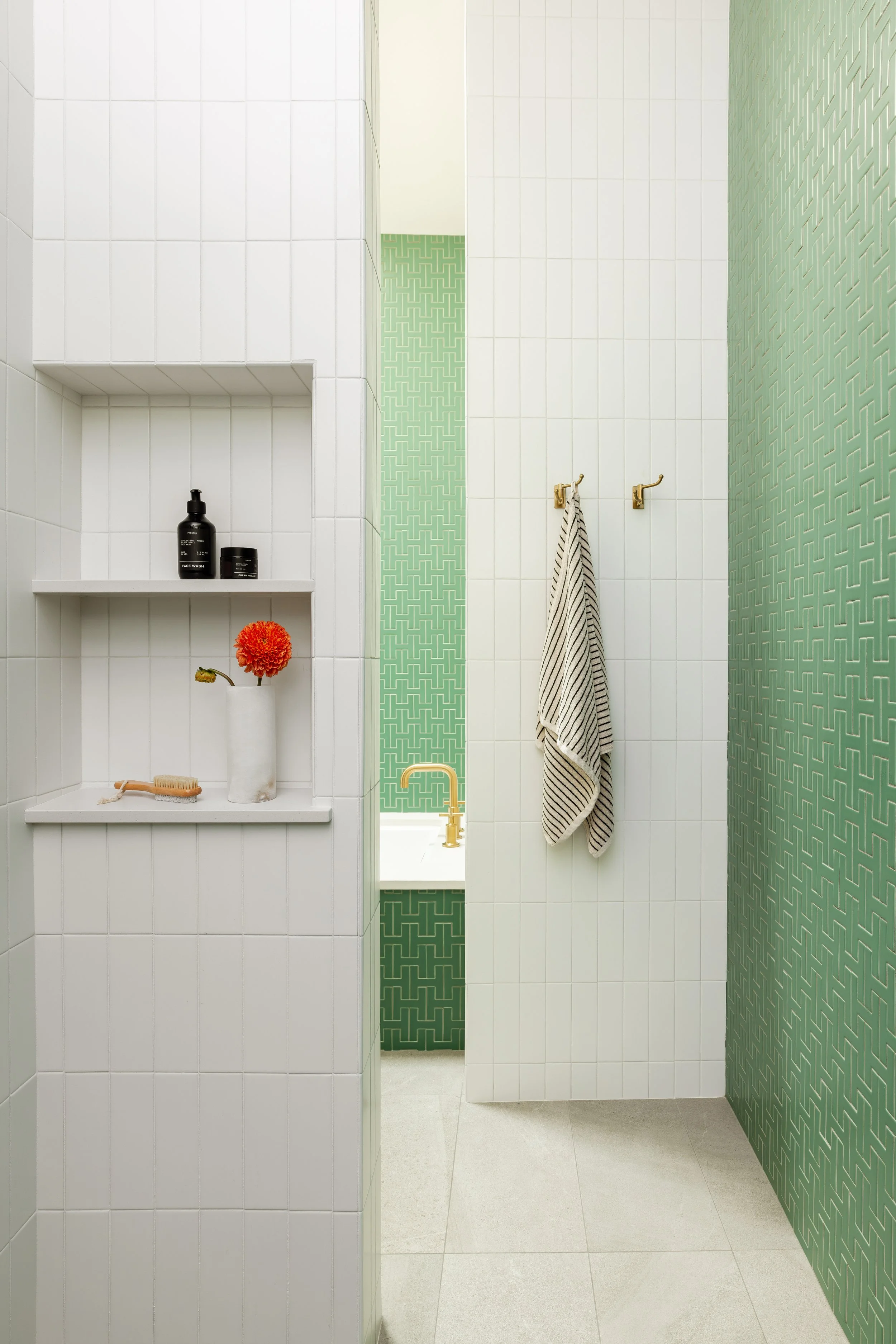 Bunk room bathroom with white and green tile and built-in shelf niches.