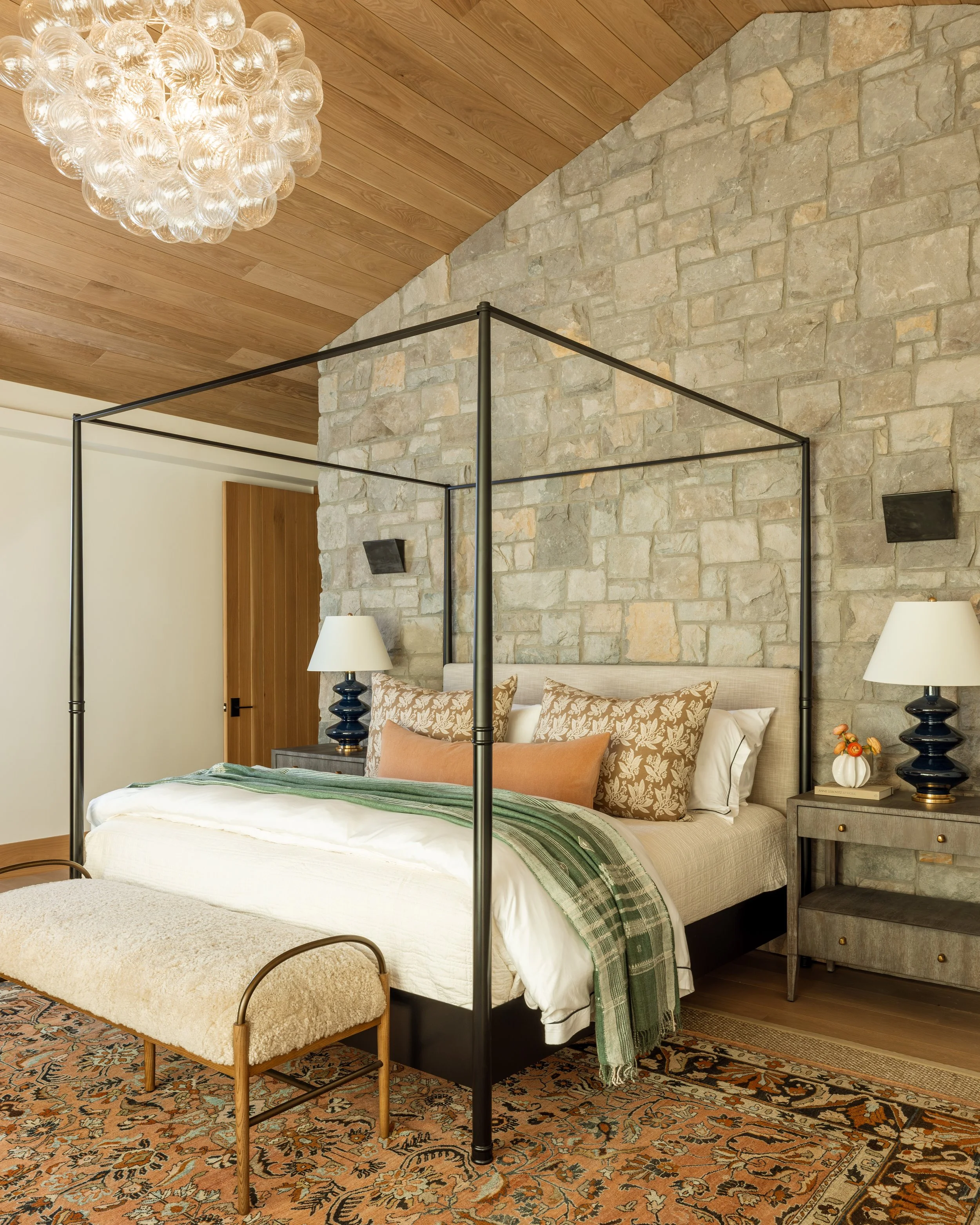 Master bedroom with a vaulted wood ceiling and stone accent wall.