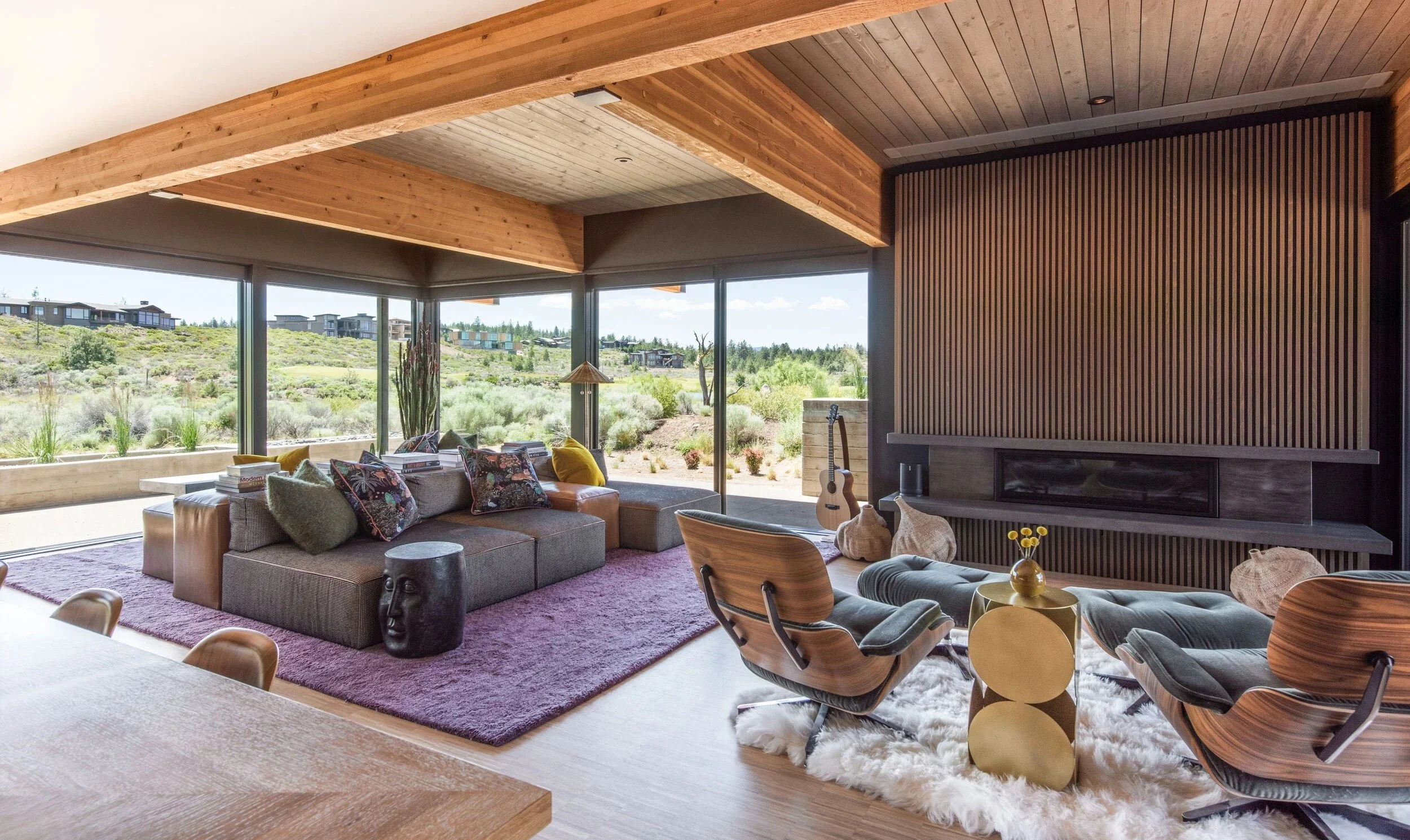 Skyfall great room with exposed wood beam ceiling, wood slat fireplace wall, and corner windows overlooking the high desert in Bend, Oregon