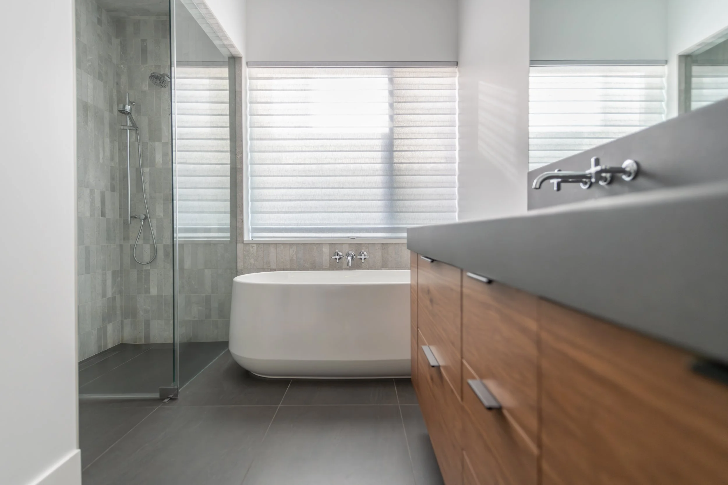 Spa-inspired modern master bathroom featuring a sleek freestanding white soaking tub, glass-enclosed walk-in shower with vertical grey tile, and a floating wood vanity in a custom Bend, Oregon home.