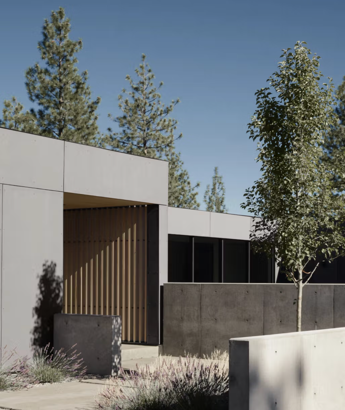 Modern custom home at dusk with illuminated interiors, dramatic angled rooflines, and warm wood detailing set among ponderosa pines — Bend Hideaway by Feldman Architecture, built by Copperline Homes in Bend, Oregon, featured in Plain Magazine