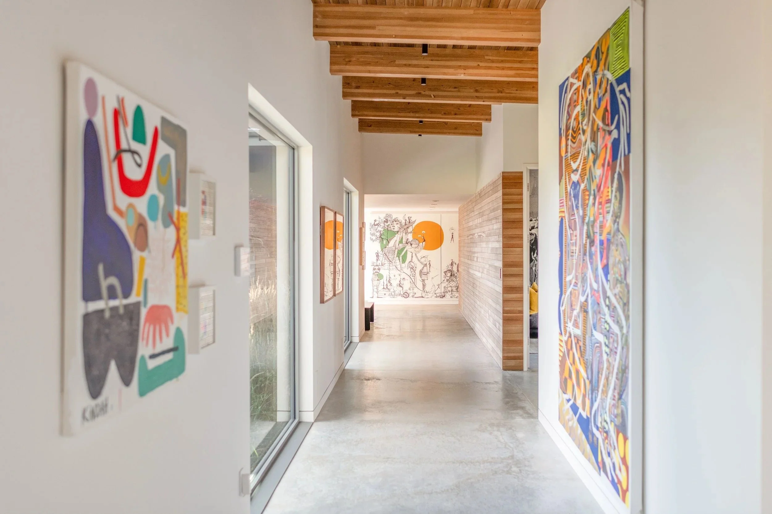 HoMA gallery hallway with polished concrete floors, wood beam ceiling, and colorful contemporary artwork in a Bend, Oregon custom home