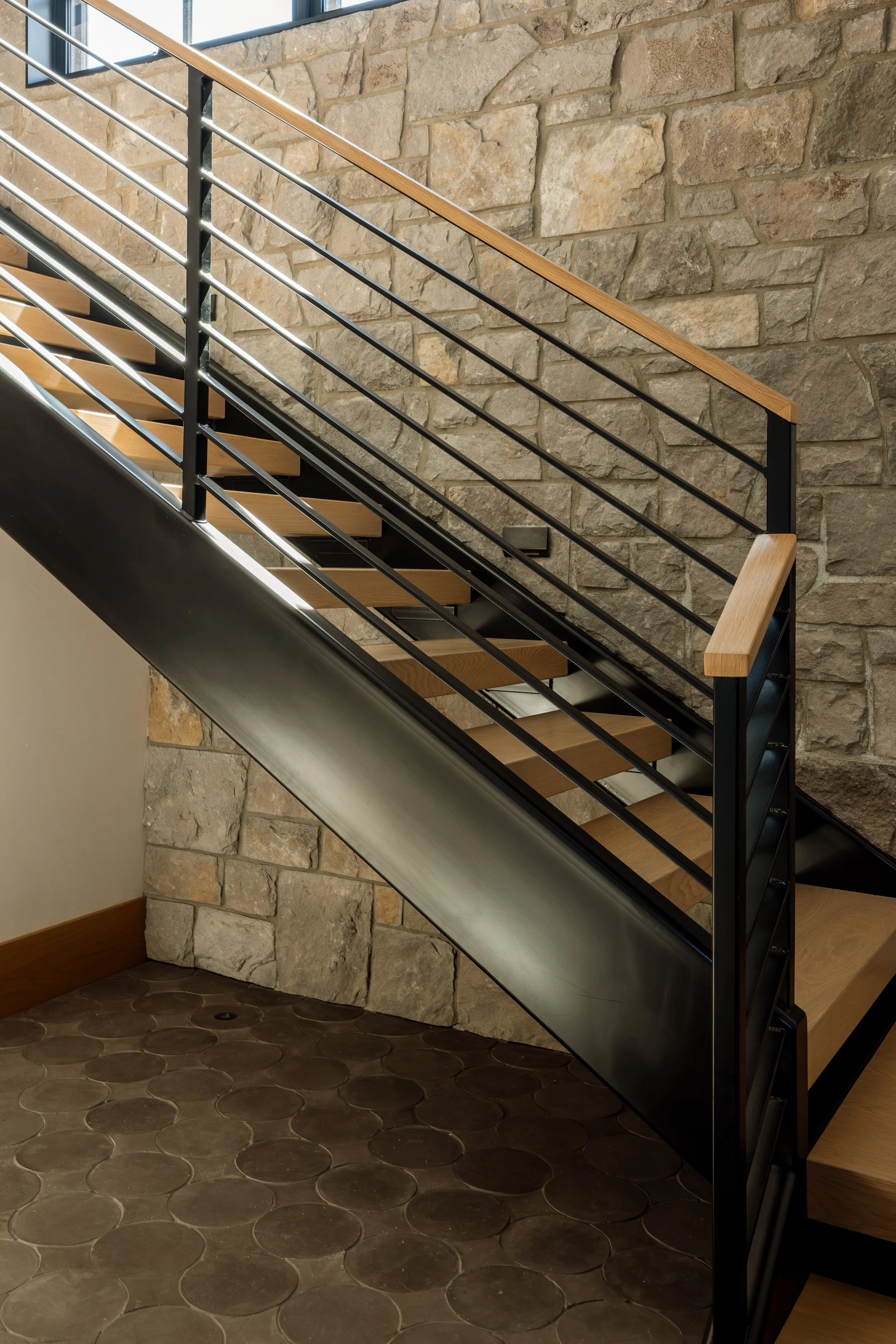 Steel stair with wood treads set against a stacked stone wall.