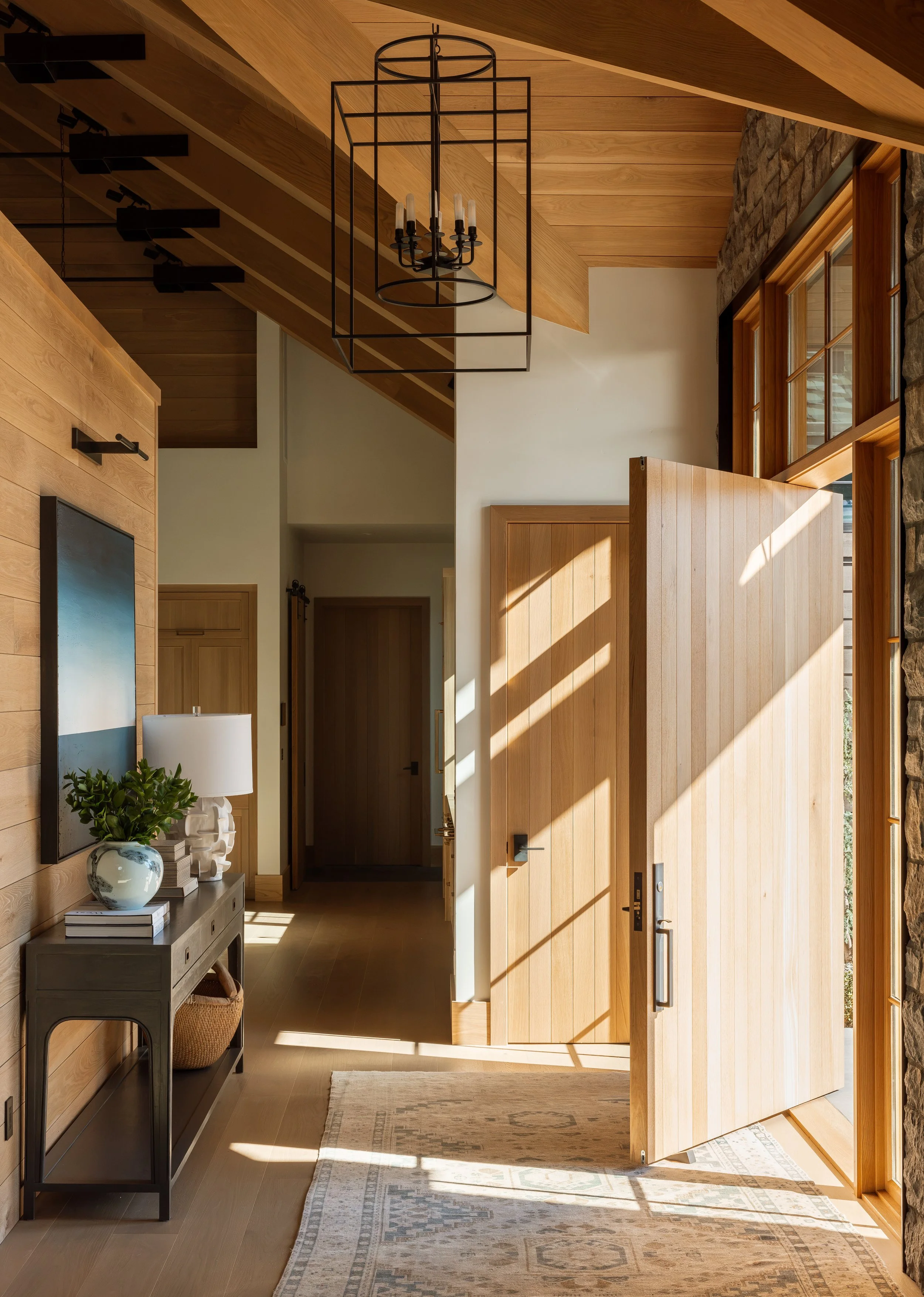 Entry hall with the pivot door swung open, wood-paneled walls and a lantern pendant.