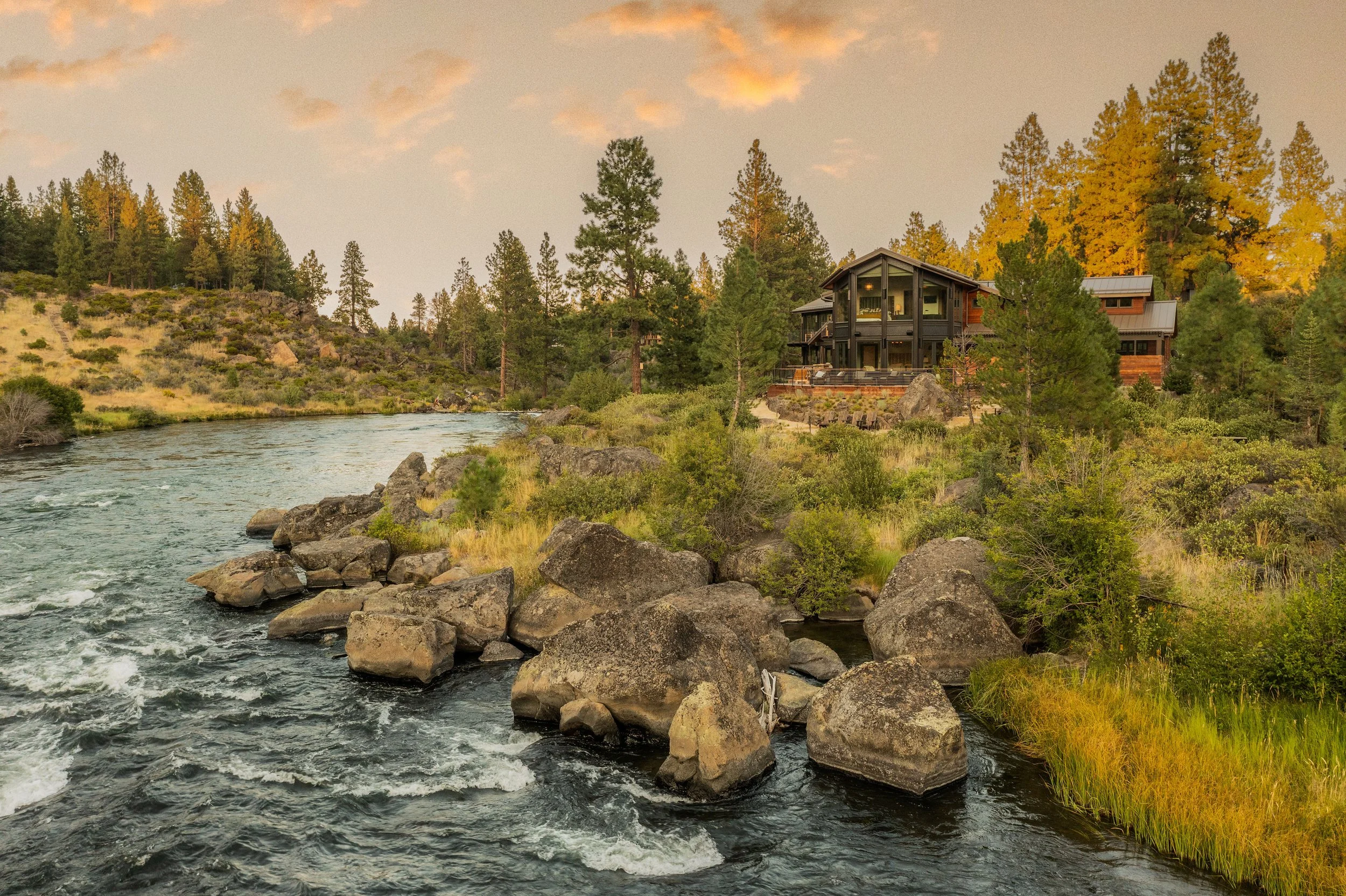 Exterior view of a multi-story luxury custom home built on the rocky banks of the Deschutes River in Bend, Oregon, featuring large windows and Northwest contemporary architecture.