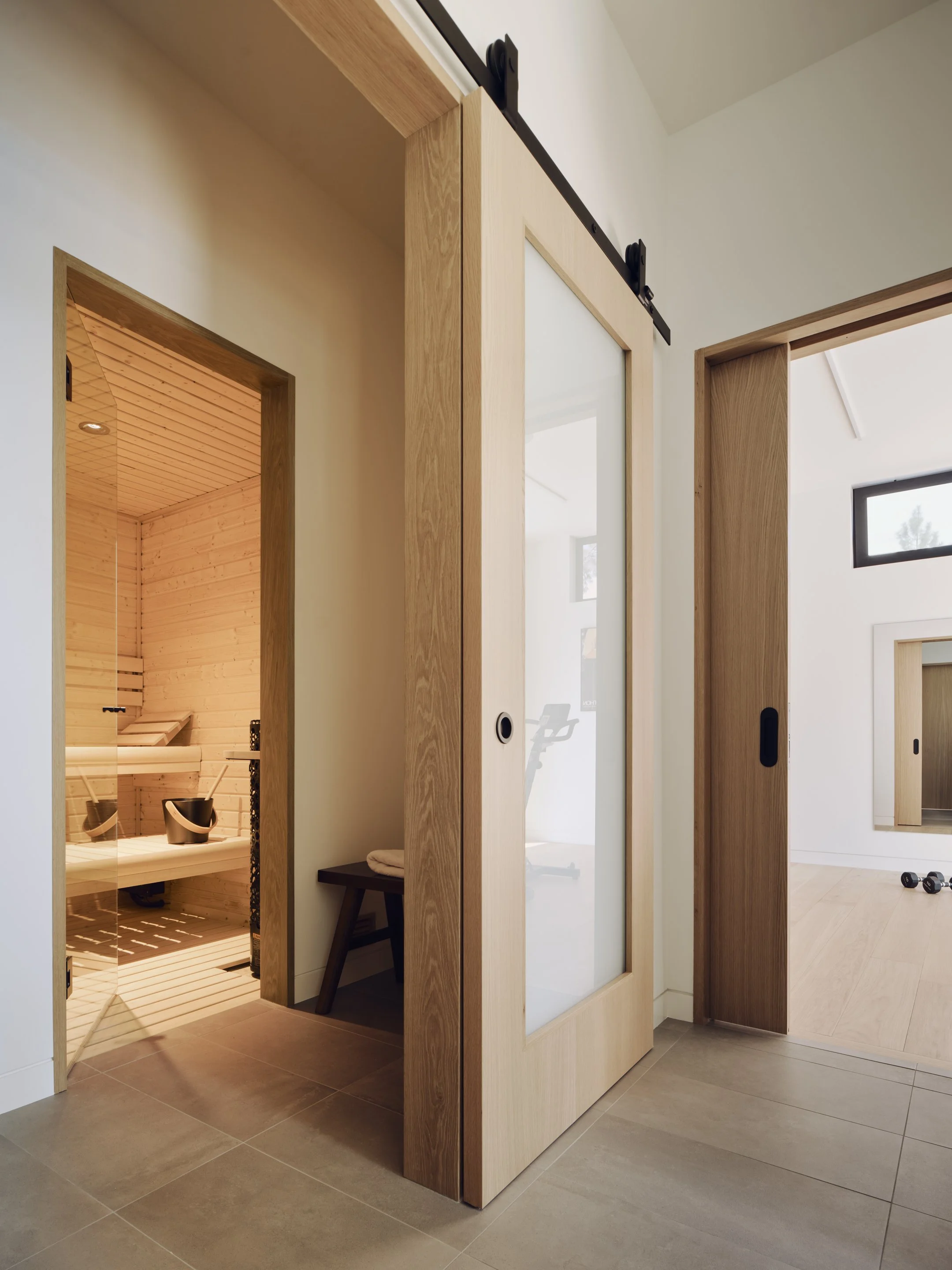 A modern interior with wooden sliding doors, leading to a sauna and a fitness area with dumbbells and a treadmill.