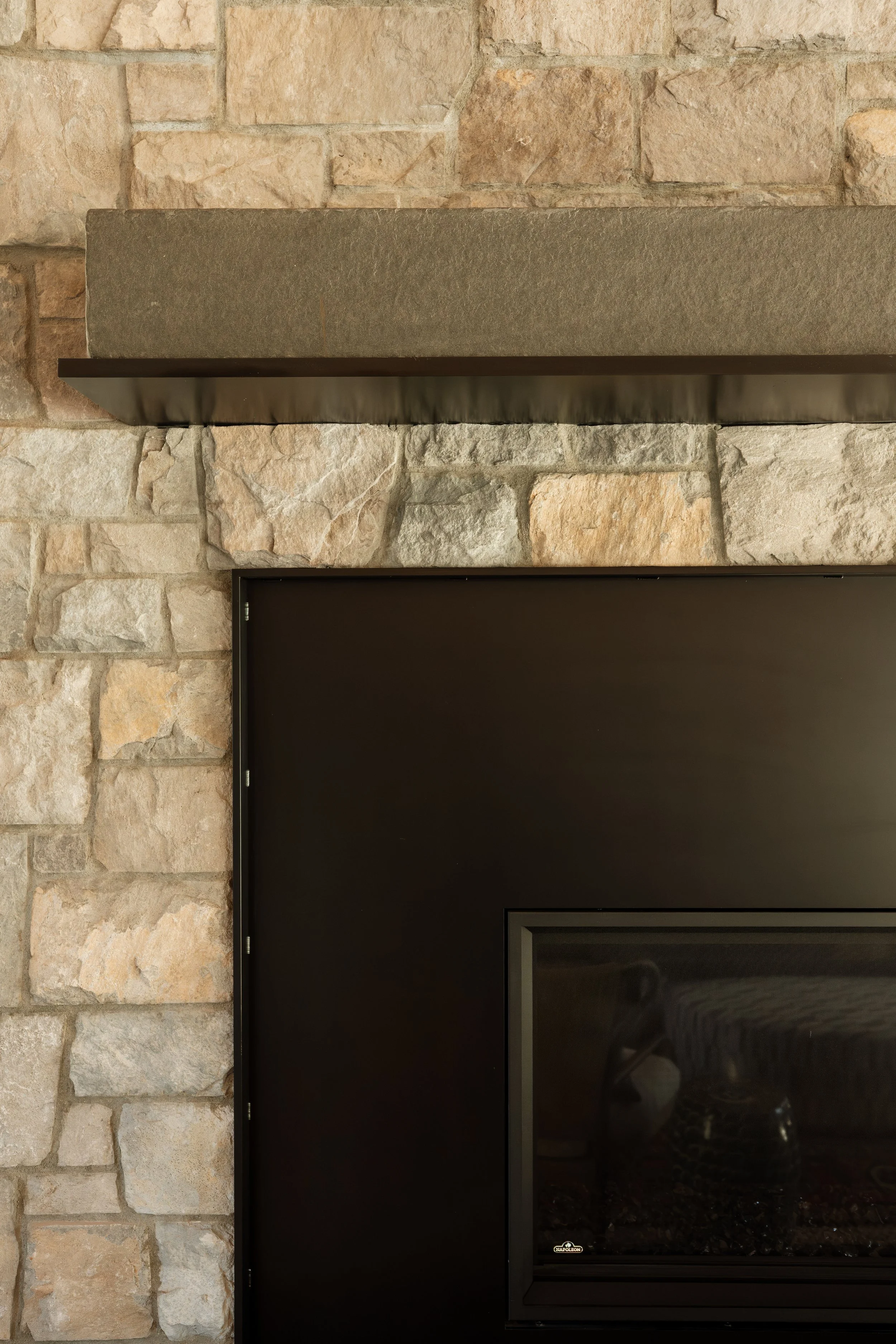 Close-up of the stacked stone fireplace with a stone mantel and black surround.