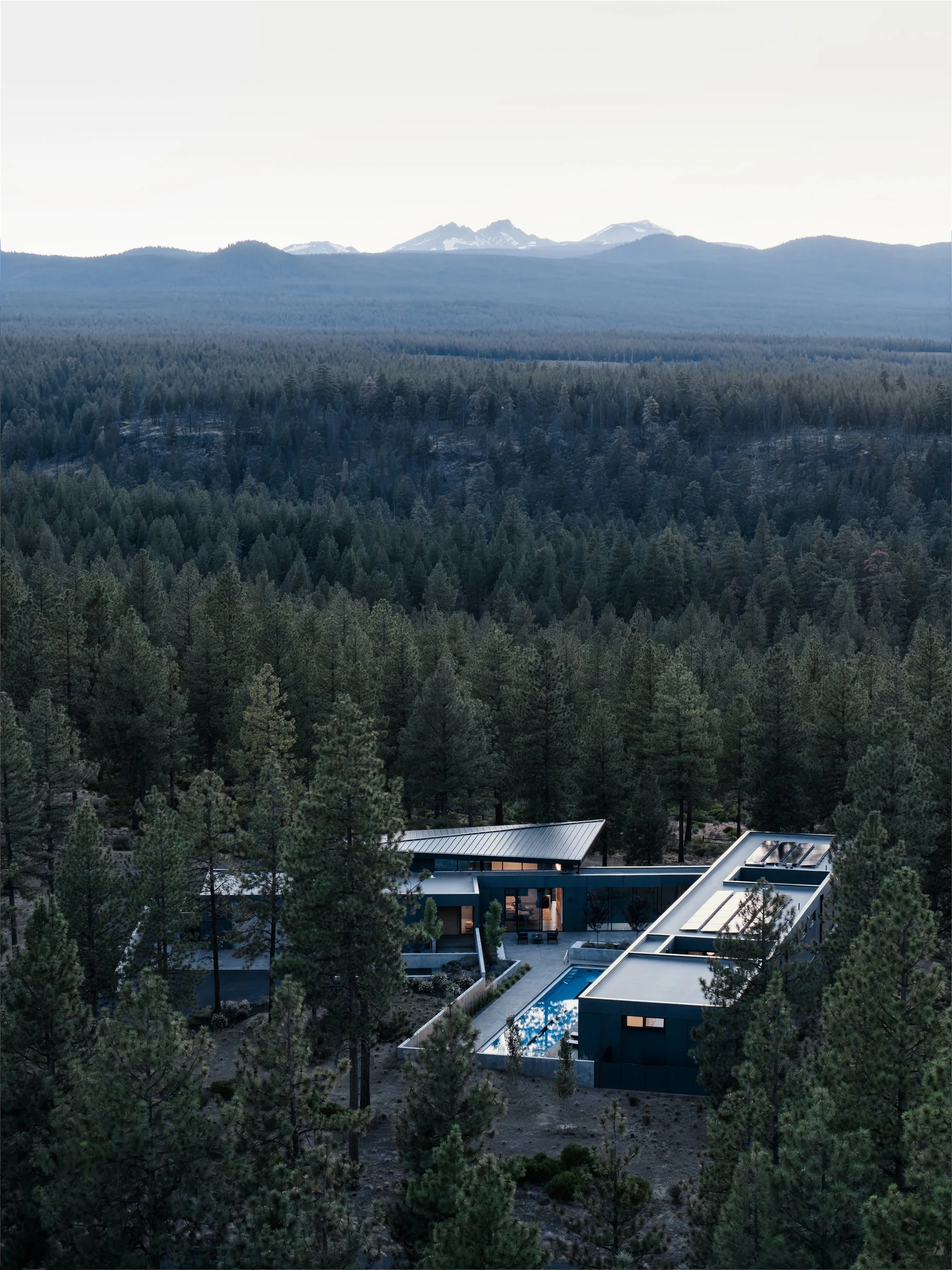 Modern house with pool in a forested mountain area under a cloudy sky.