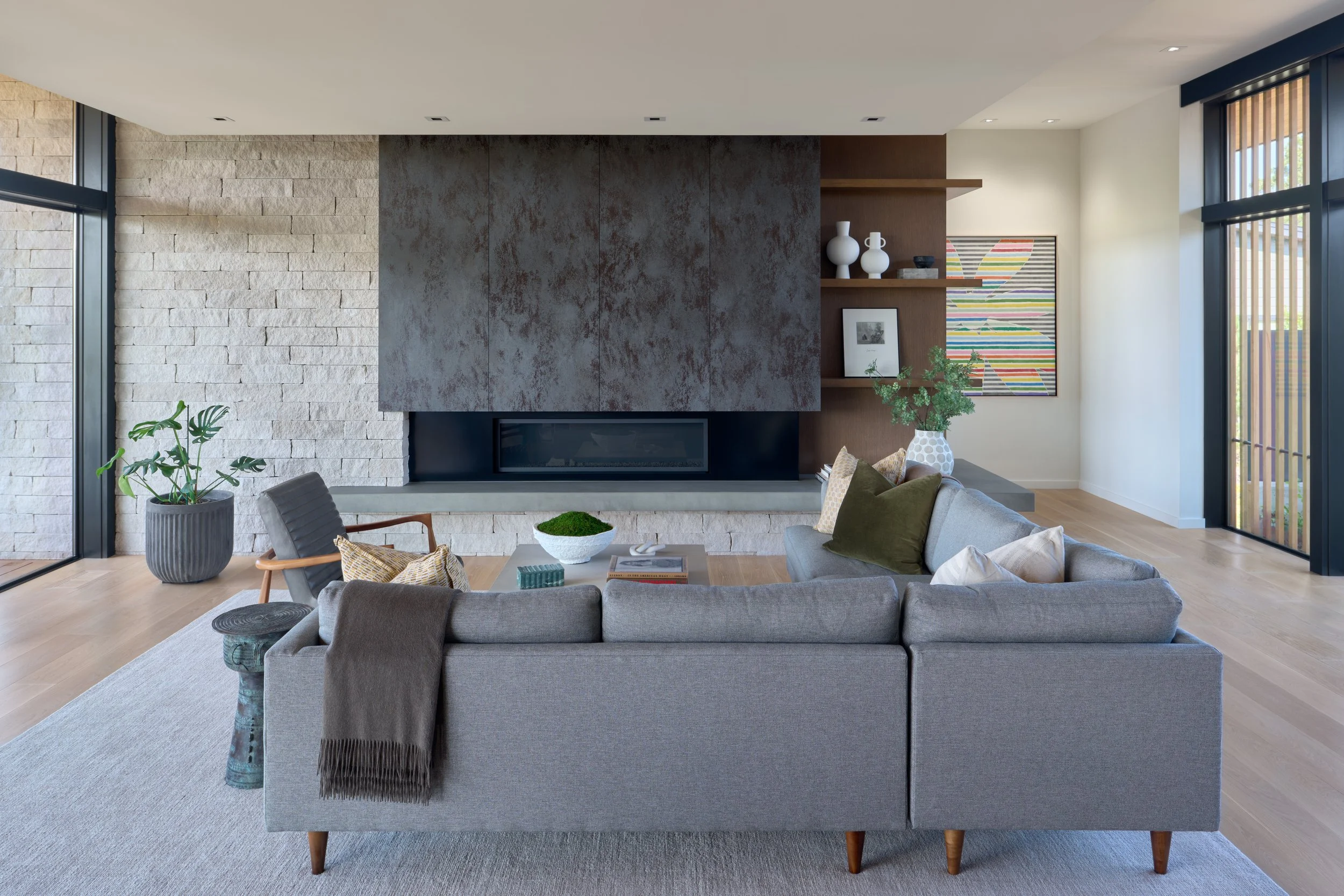 Modern living room with linear gas fireplace, white stone accent wall, built-in wood shelving, and gray sectional sofa in a Bend Oregon custom home