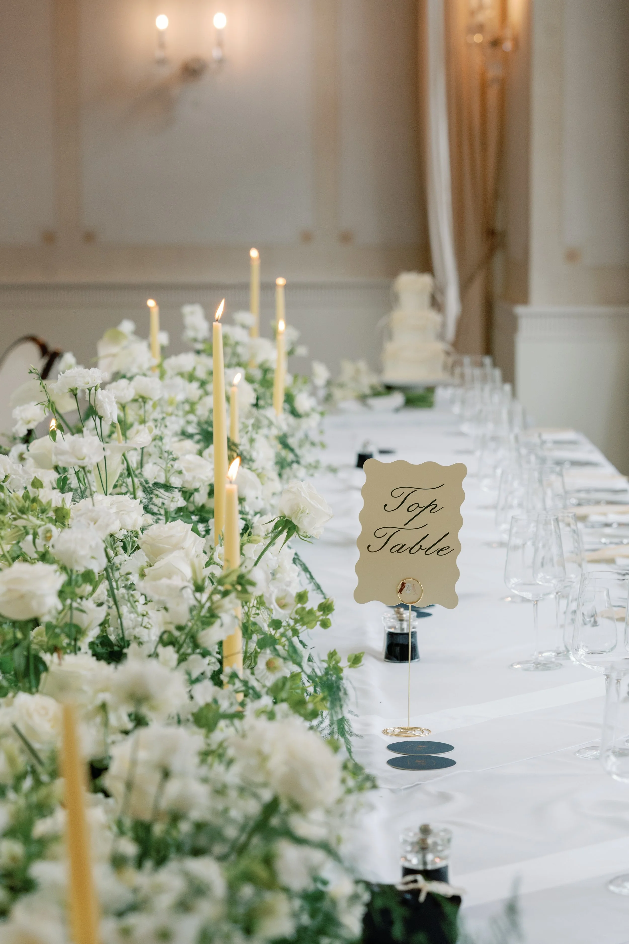 Elegant banquet table decorated with white flowers and tall candles, with a sign indicating 'Top Table' at a formal event or wedding reception.