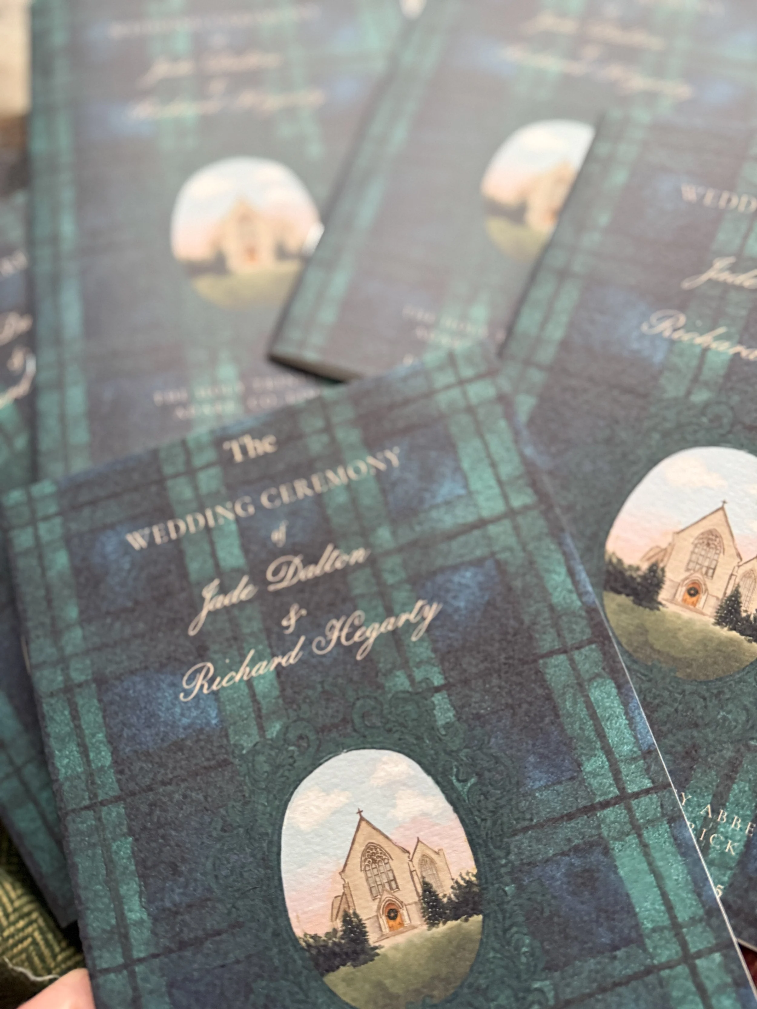 Wedding program booklets with a dark green plaid pattern, featuring an illustration of a church and the text 'The Wedding Ceremony of Jade Dalton & Richard Hegarty'.