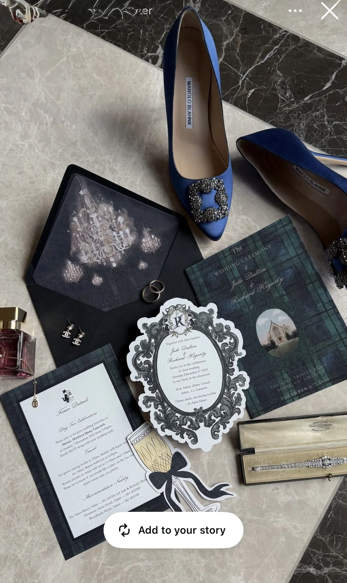 Blue high-heeled shoes with rhinestone embellishments and a decorative buckle, wedding invitation cards, wedding rings, earrings, perfume bottle, and a jewelry box arranged on a surface, likely for a wedding preparation or event.