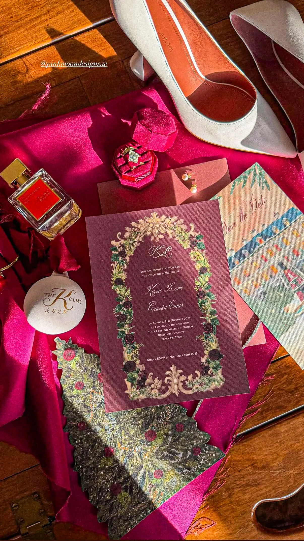 Wedding invitation, jewelry box, perfume bottle, earrings, candle, and Christmas decorations arranged on pink fabric.