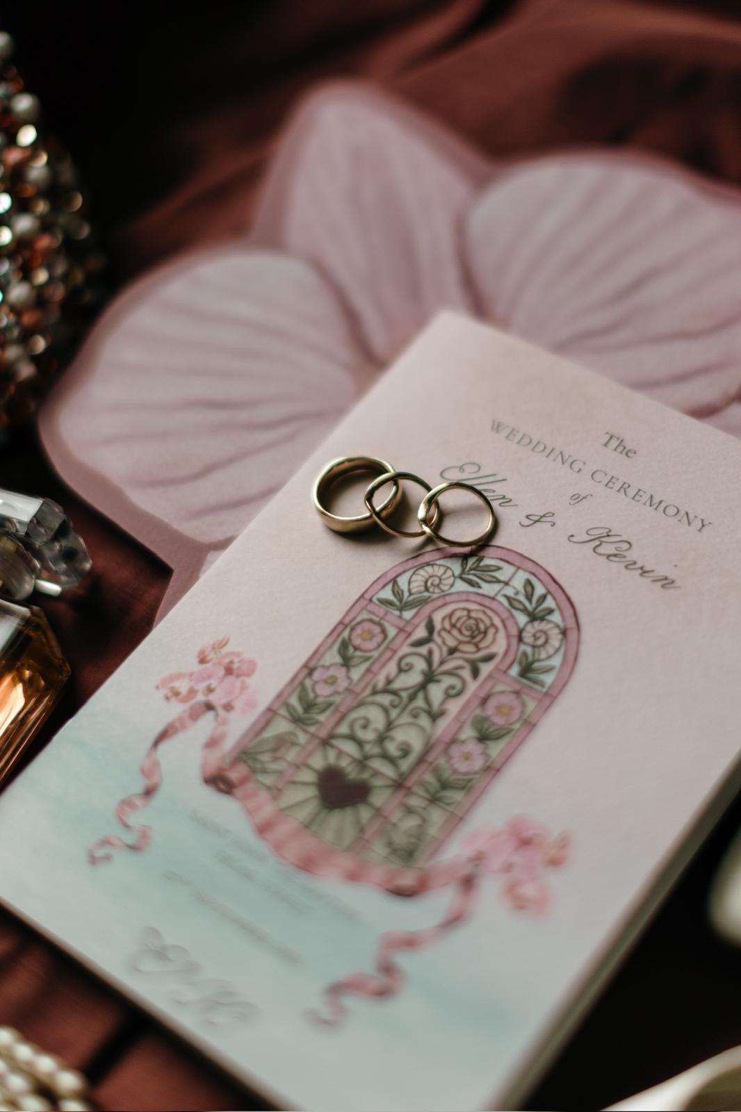 Wedding invitation with three wedding rings placed on top, decorated with floral illustrations and pink ribbons