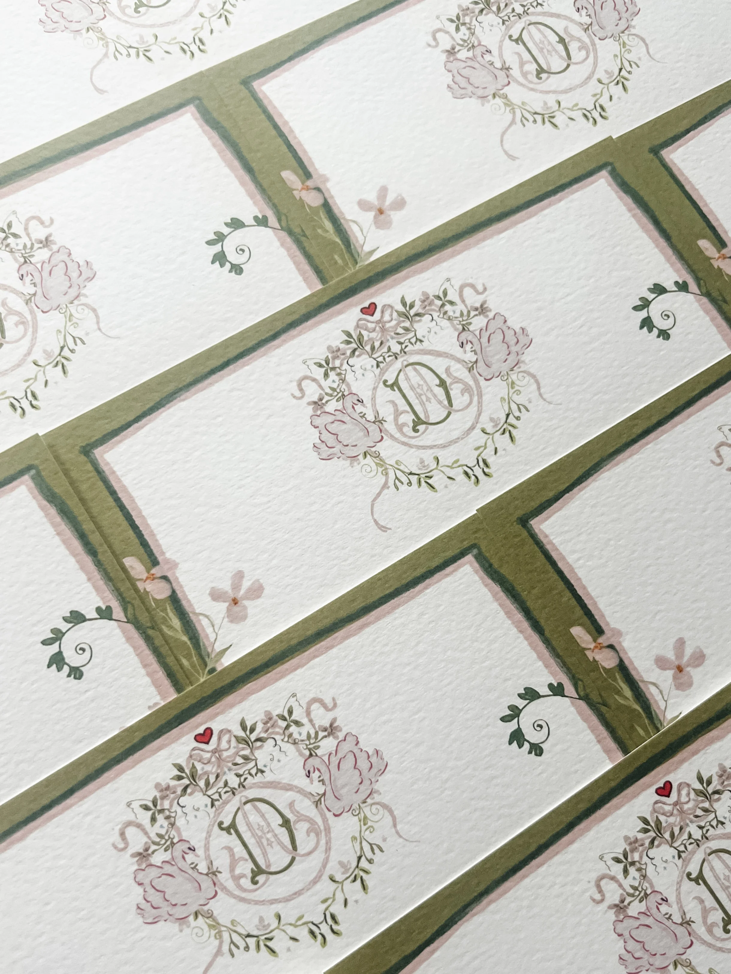 Close-up of decorative paper with floral motifs, monograms, and heart accents, arranged in a grid pattern with green and pink borders.