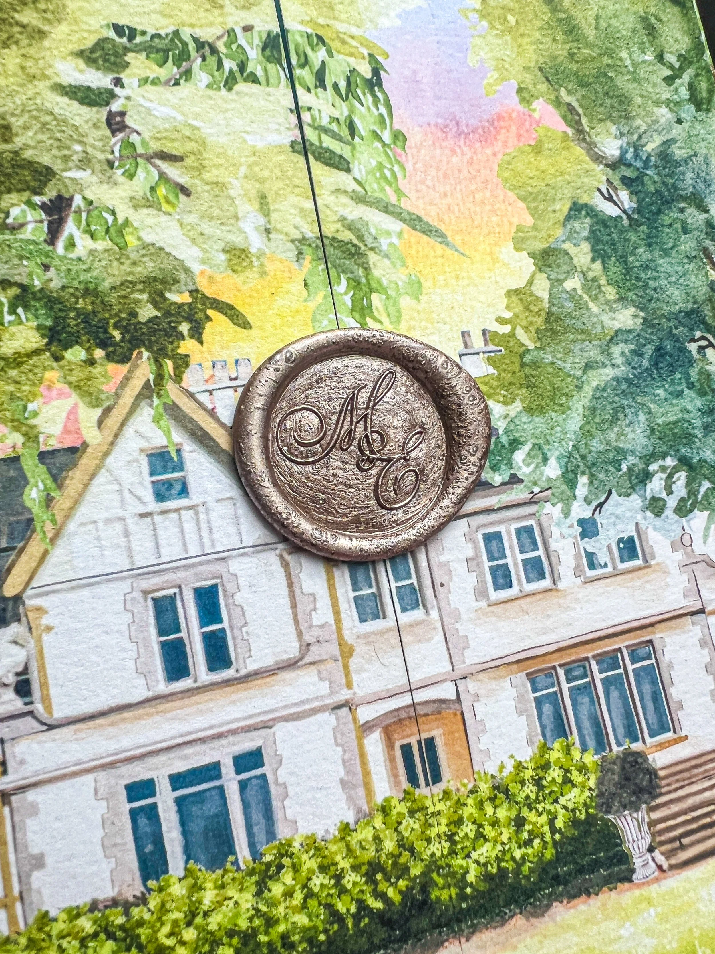 A decorative wax seal with the monogram 'M E' placed on a colorful illustration of a large house surrounded by trees and greenery.
