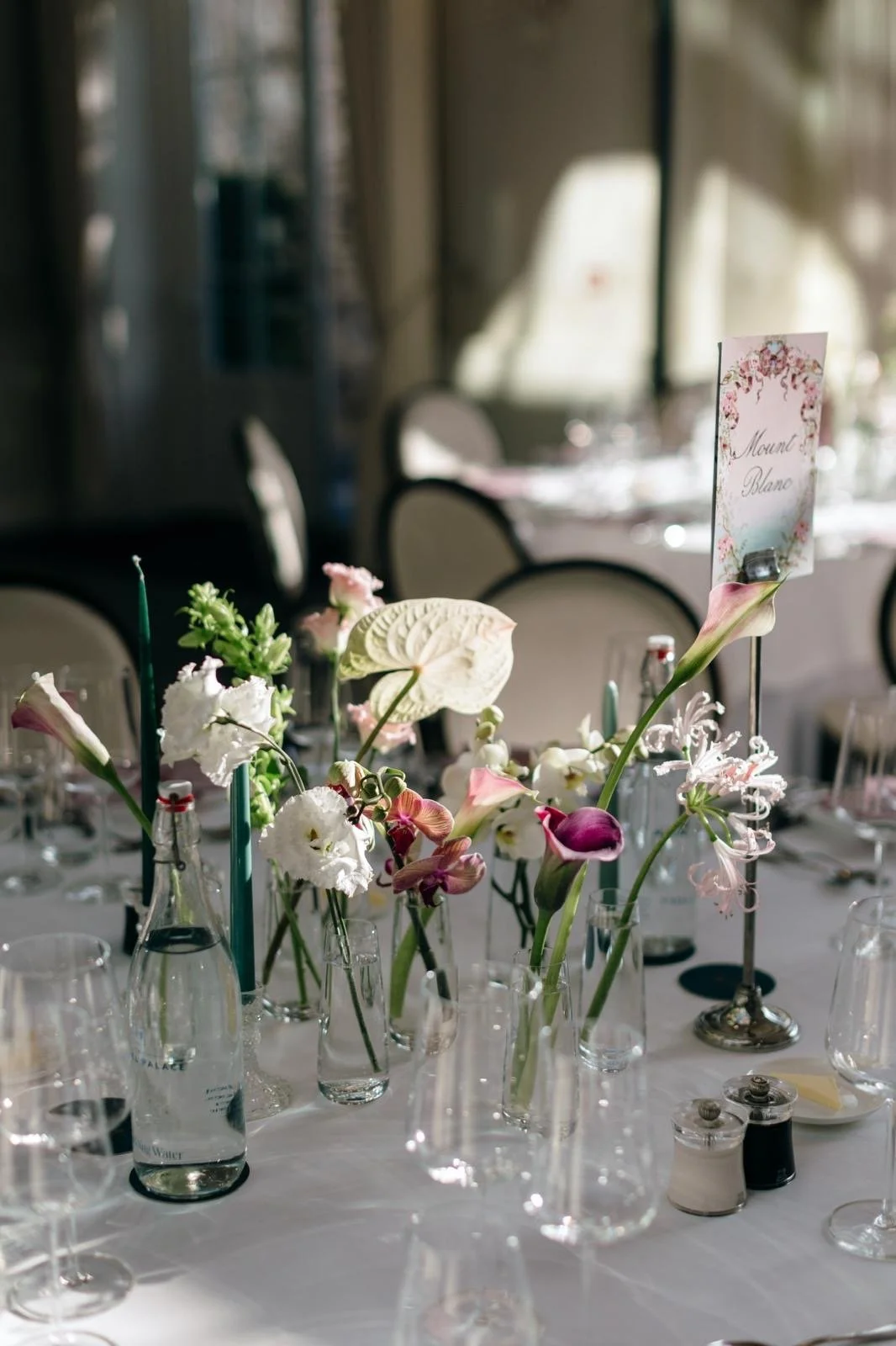 Elegant banquet table with floral centerpiece, glass bottles, and place settings, in a decorated event space.