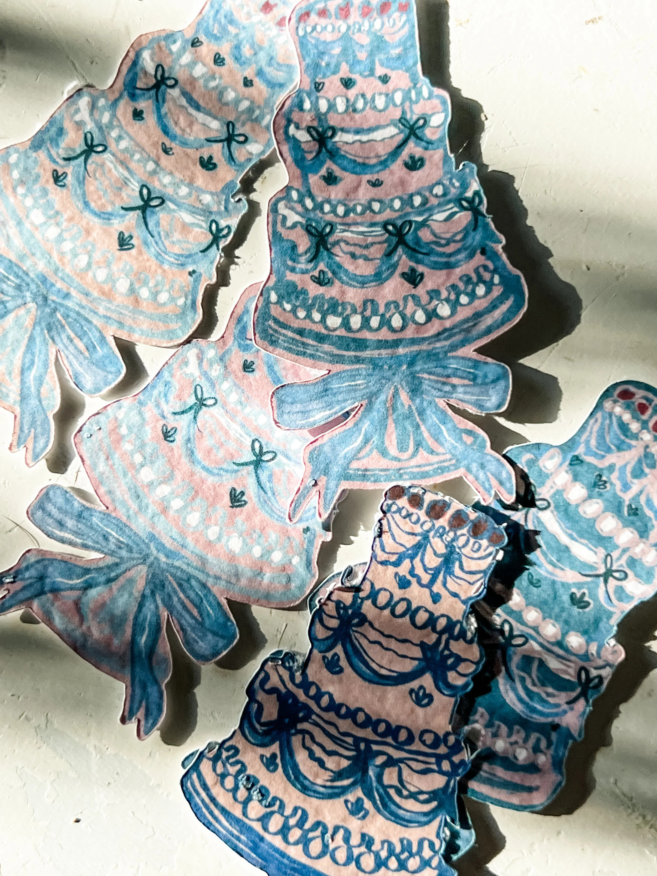 Multiple colorful paper cutouts of tiered cakes with bows and decorative patterns, layered and arranged on a surface.