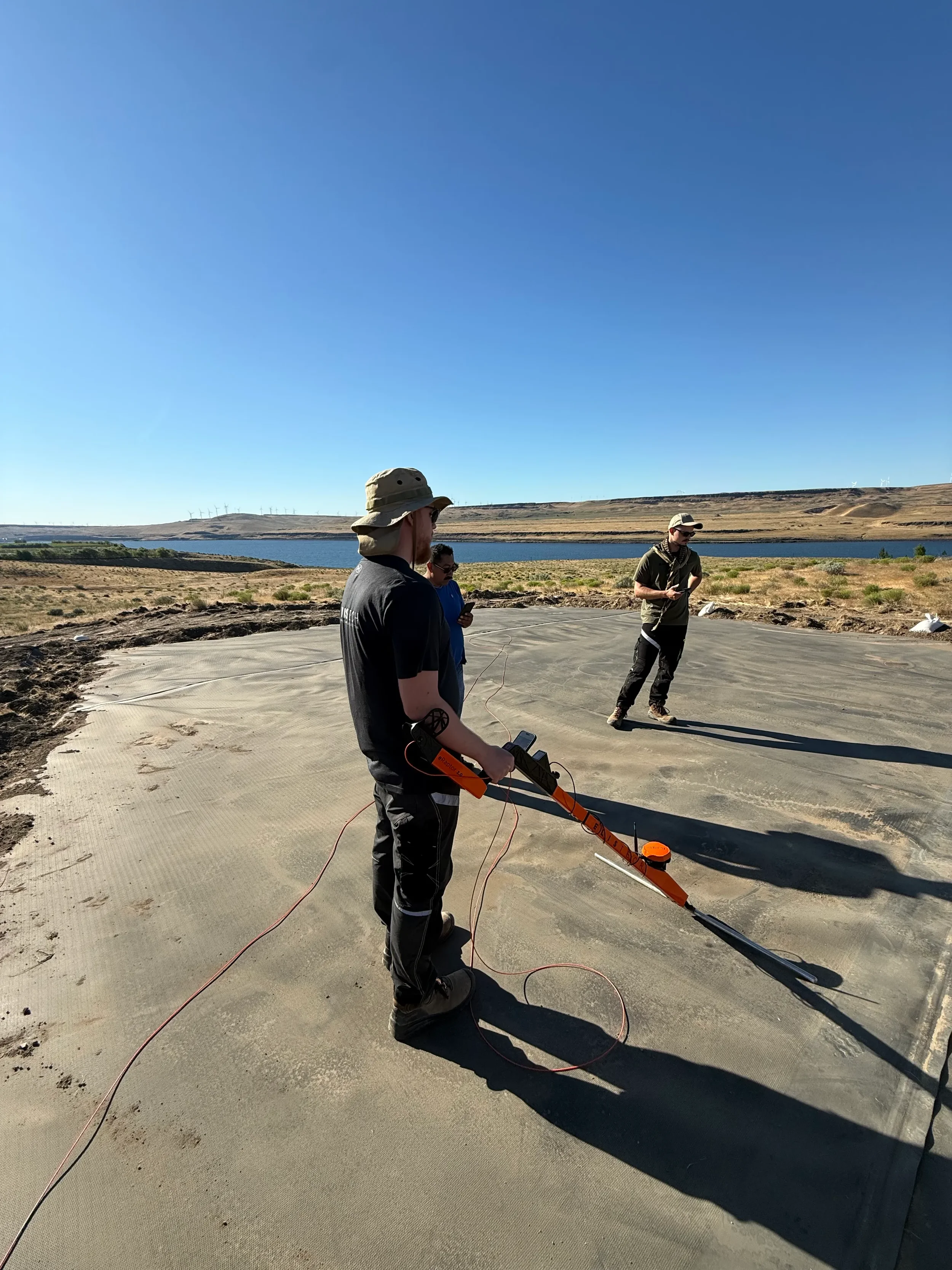 Field technician using handheld electrical leak detection probe to locate pinhole defects on geomembrane liner surface