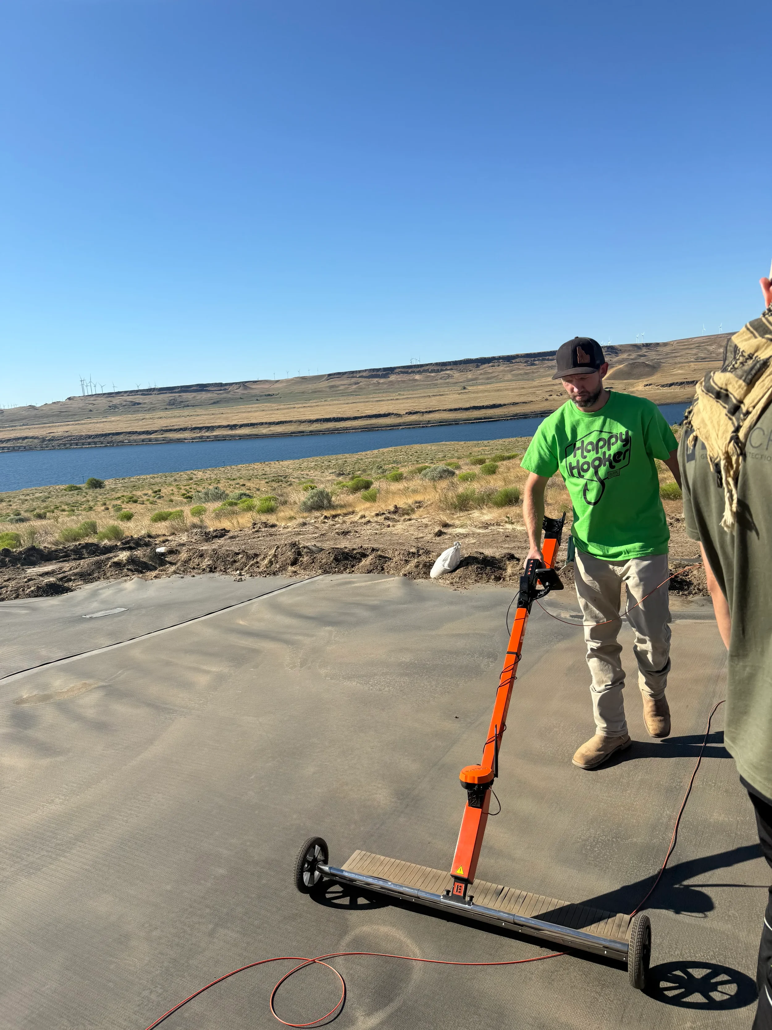 Technician operating electrical leak detection equipment on exposed geomembrane liner during ASTM-compliant ELL survey