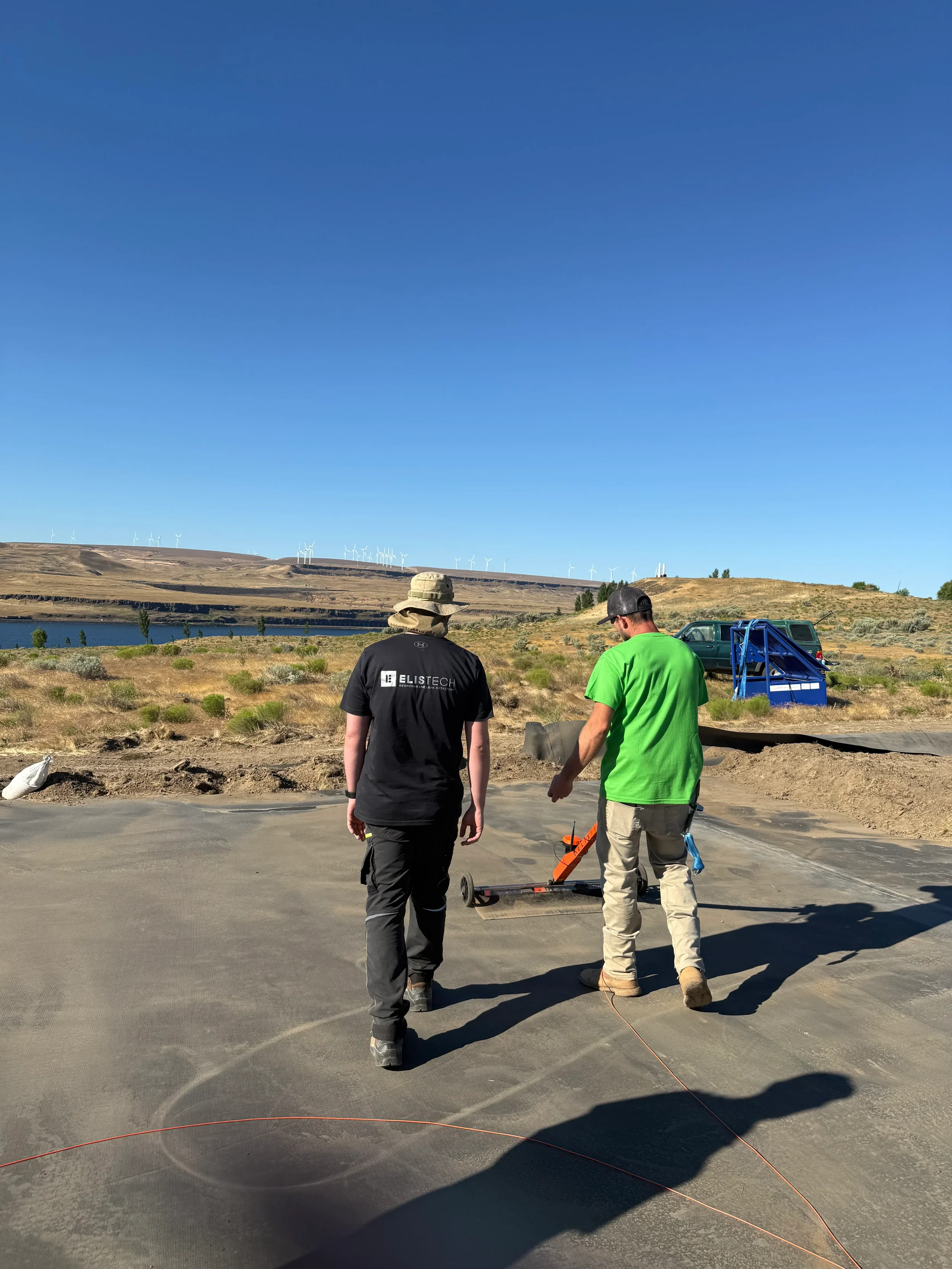 Geosynthetic Advisors leak detection team inspecting geomembrane liner installation with electrical leak location cart at containment pond site