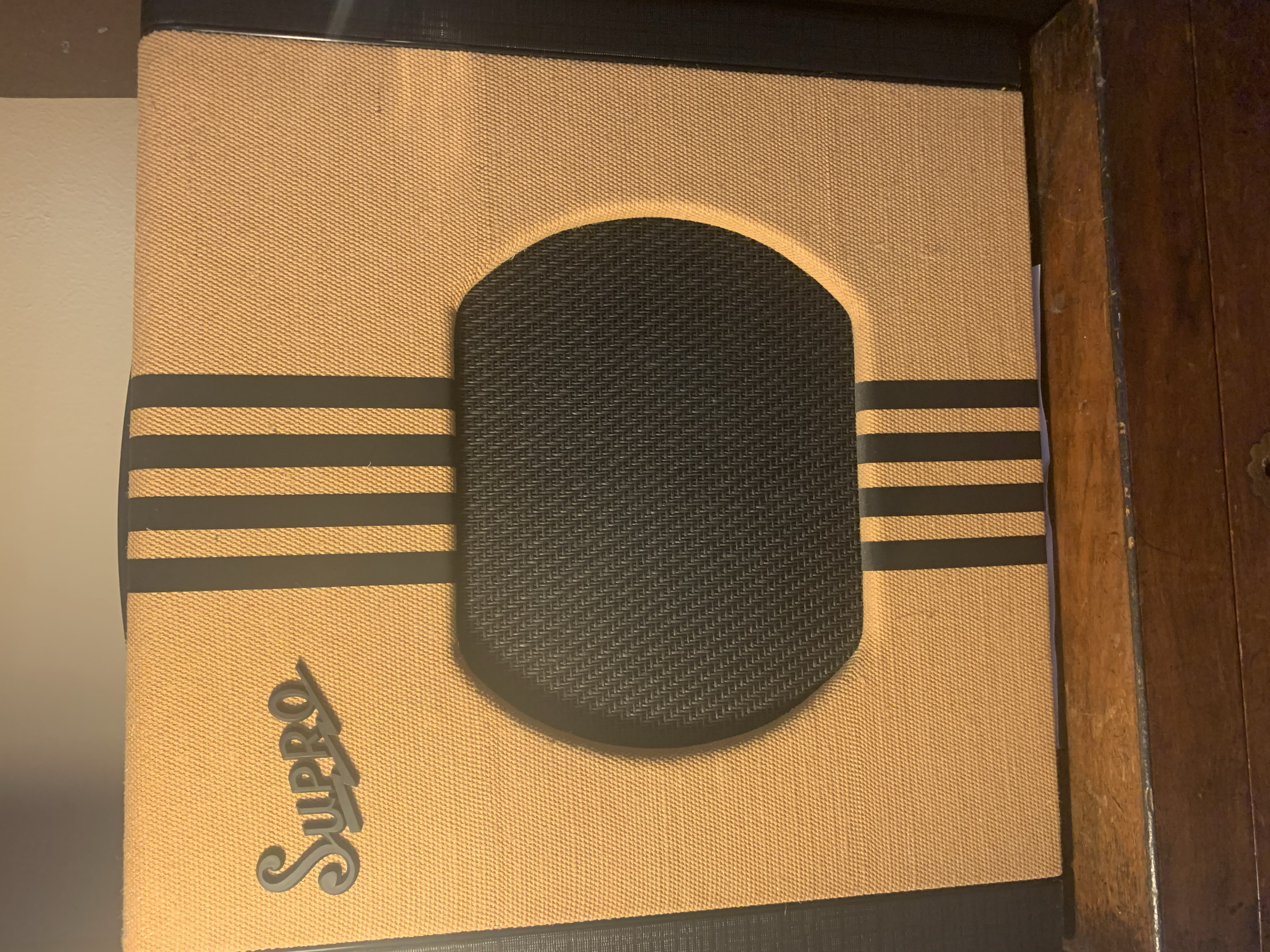 A Sunpro branded valve amp with a tan fabric cover, black grille, and horizontal black stripes, placed on a wooden surface.