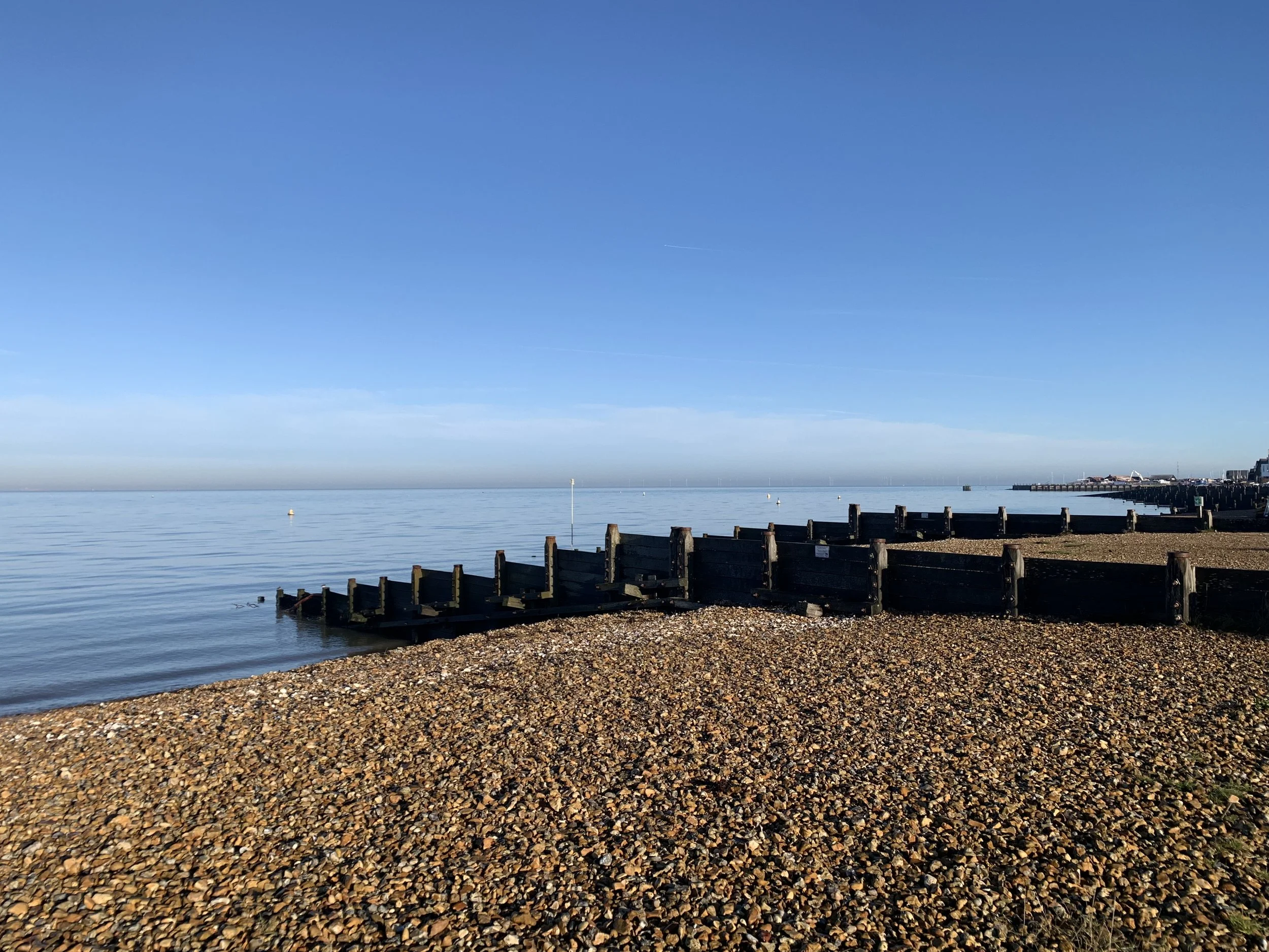 Calm sea with a pebble beach and wooden groynes under a clear blue sky