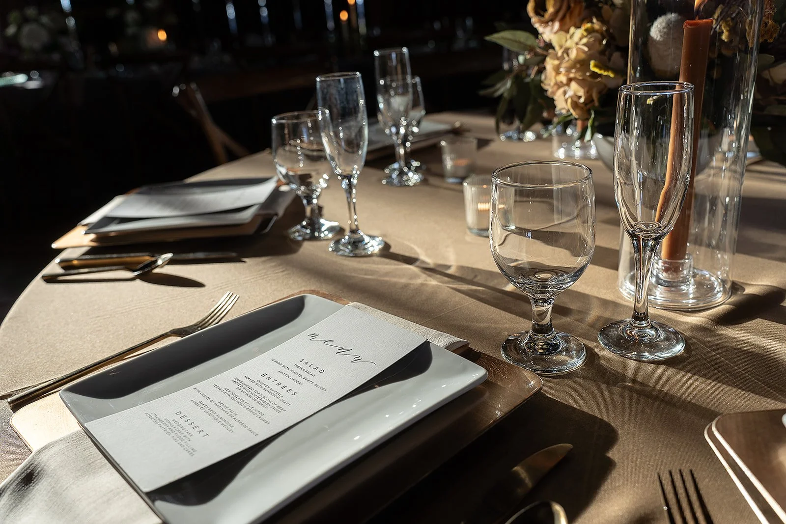 Elegant dining table set with wine glasses, water glasses, silverware, menu, and floral centerpiece in natural light at a 19th century estate