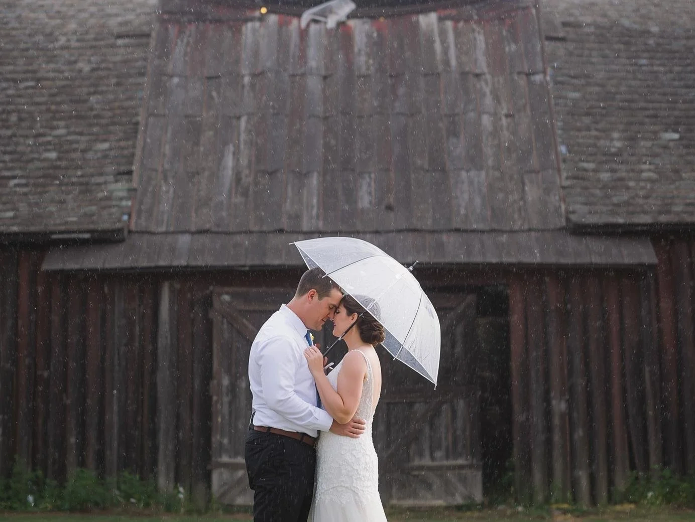 Couple under clear umbrella at Cedar Bay Farm barn, rainy weddings Ohio, romantic outdoor wedding scene