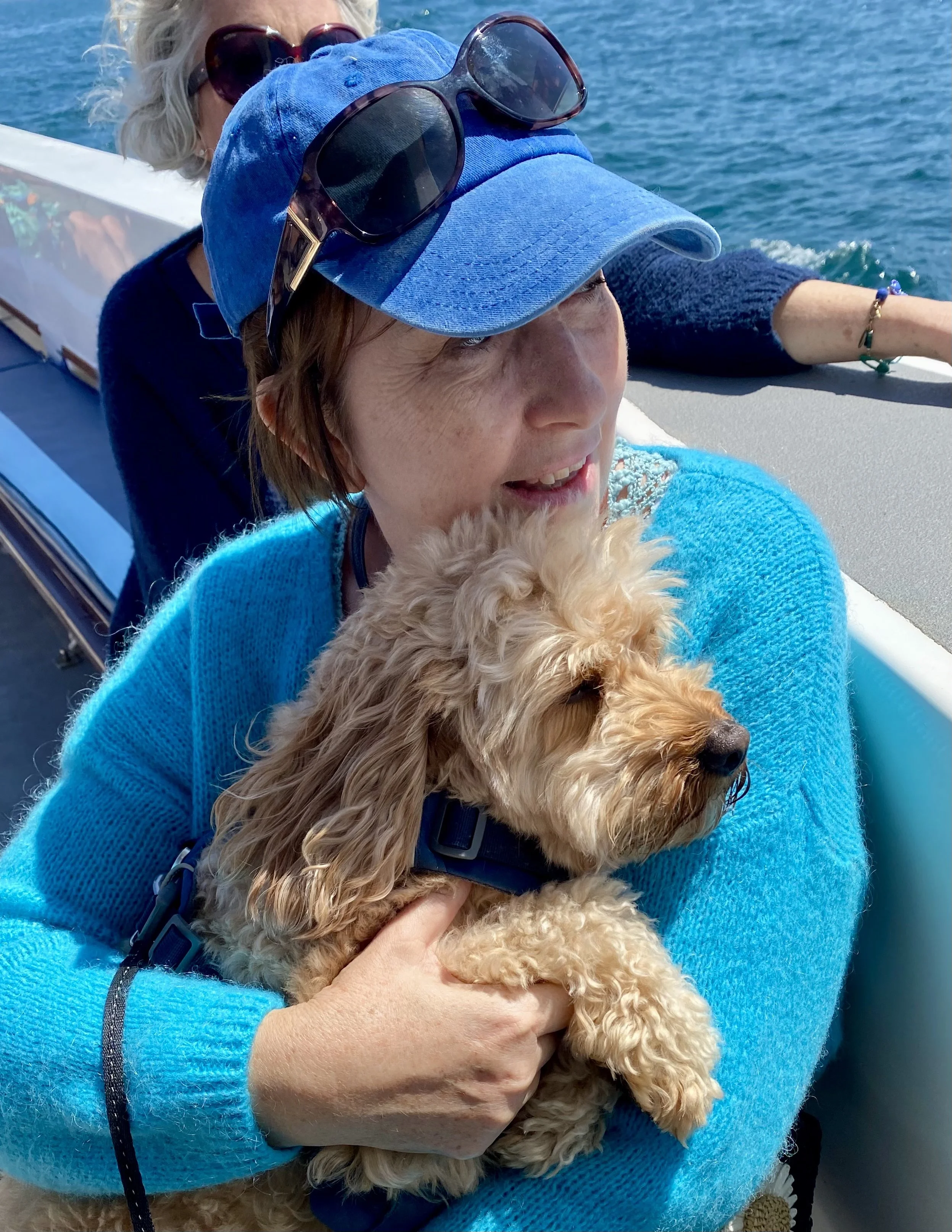 Nicky Williams is wearing a blue jumper and cap holding her dog Luca while on a boat.